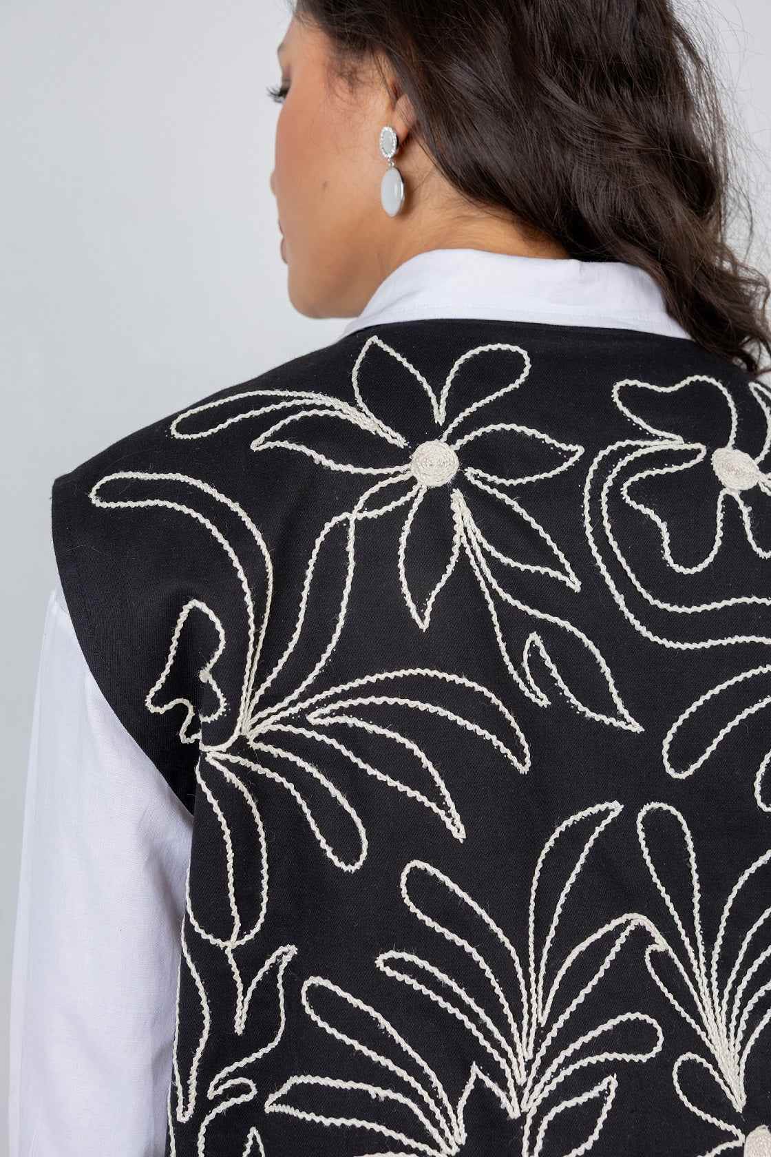 Black floral embroidered vest worn by a person on a plain background