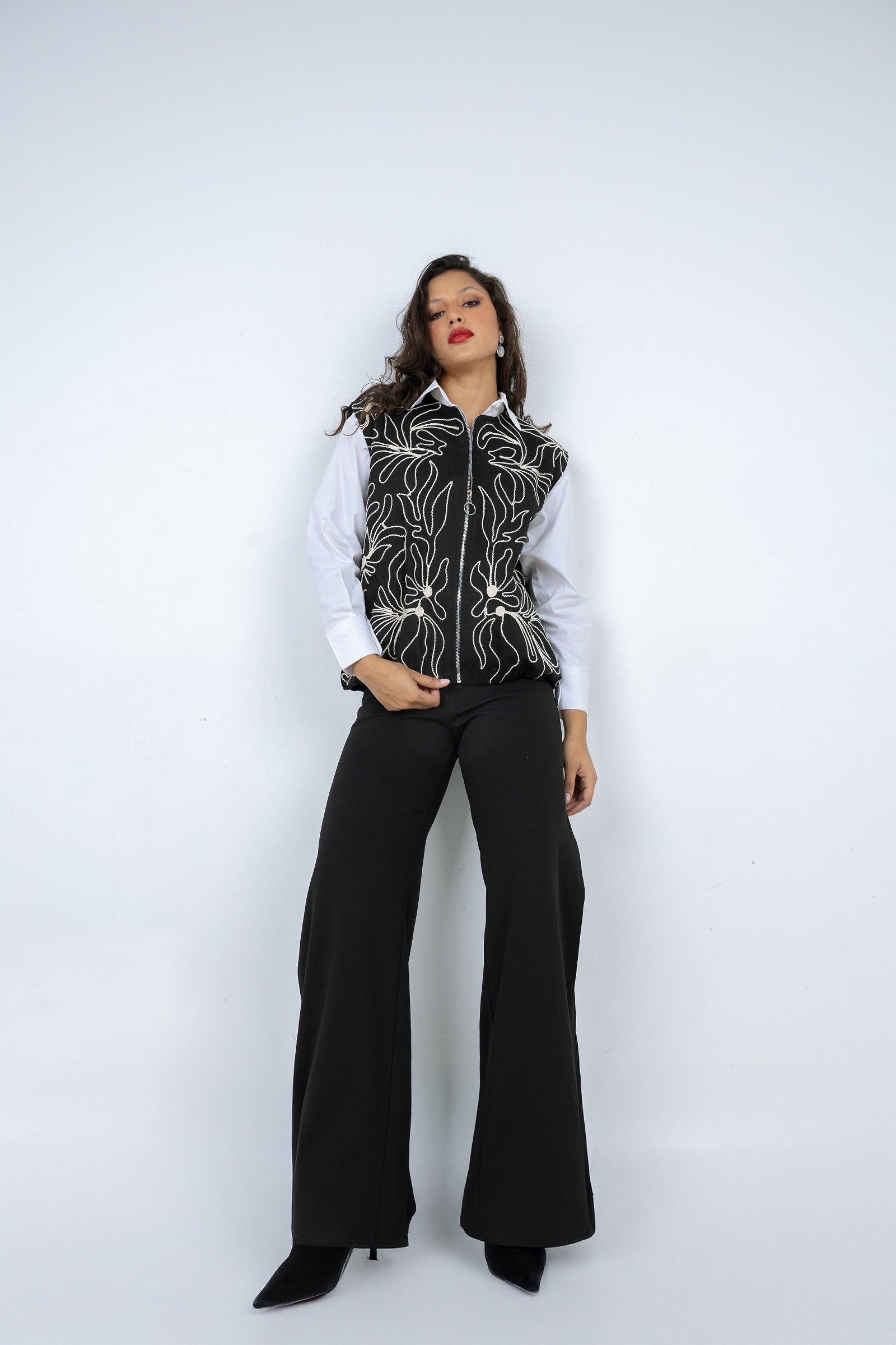 Person wearing a black and white patterned vest over a white shirt with black flared pants on a white background