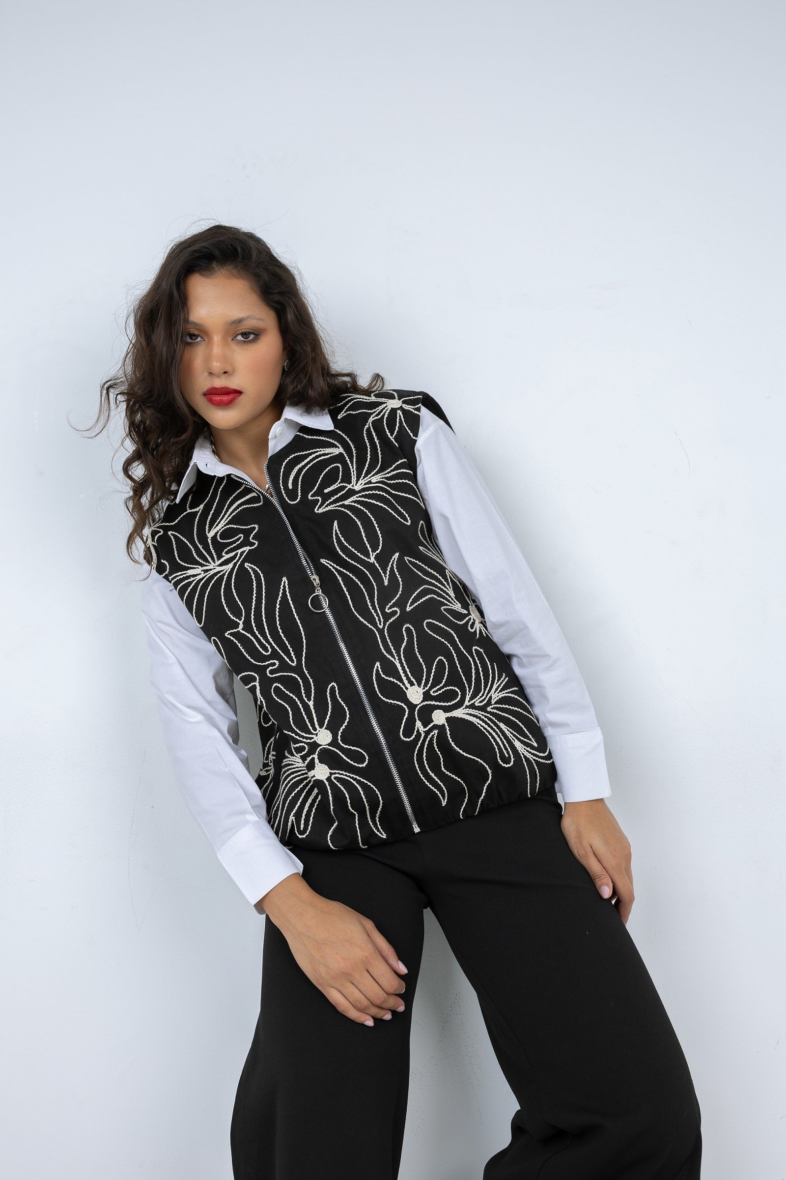 Woman wearing a black floral-patterned vest over a white shirt on a white background