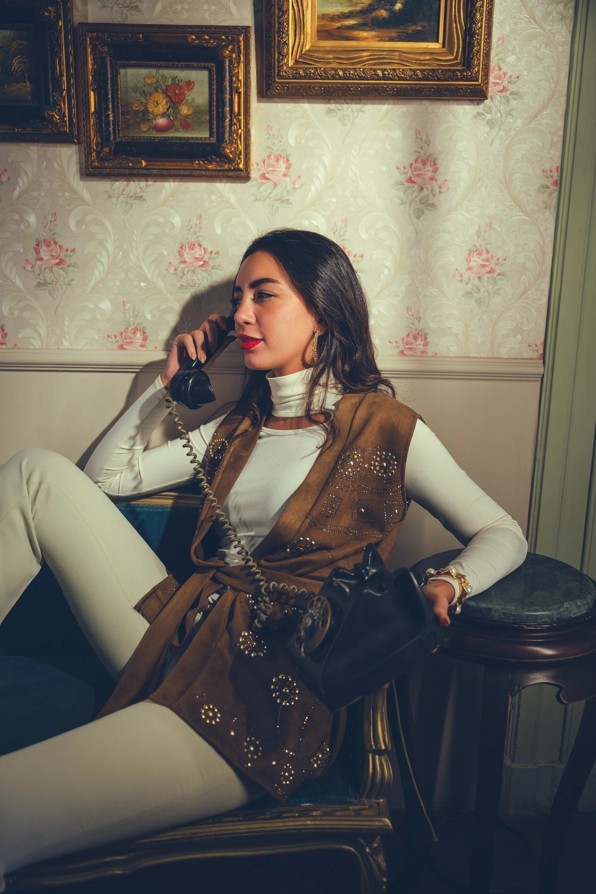 Woman sitting in a vintage-style room, talking on a phone.