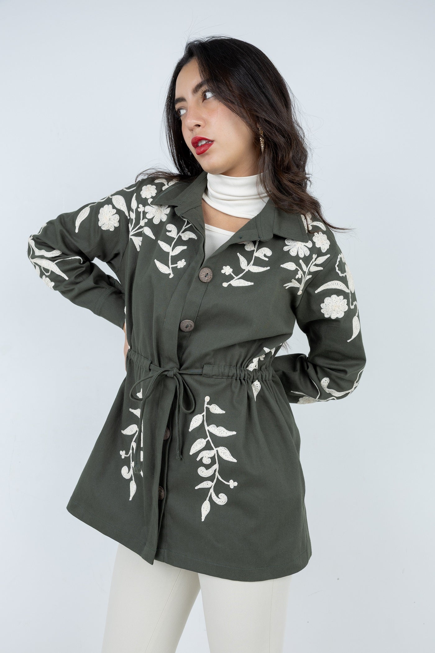 Woman wearing a green jacket with white floral patterns on a plain background