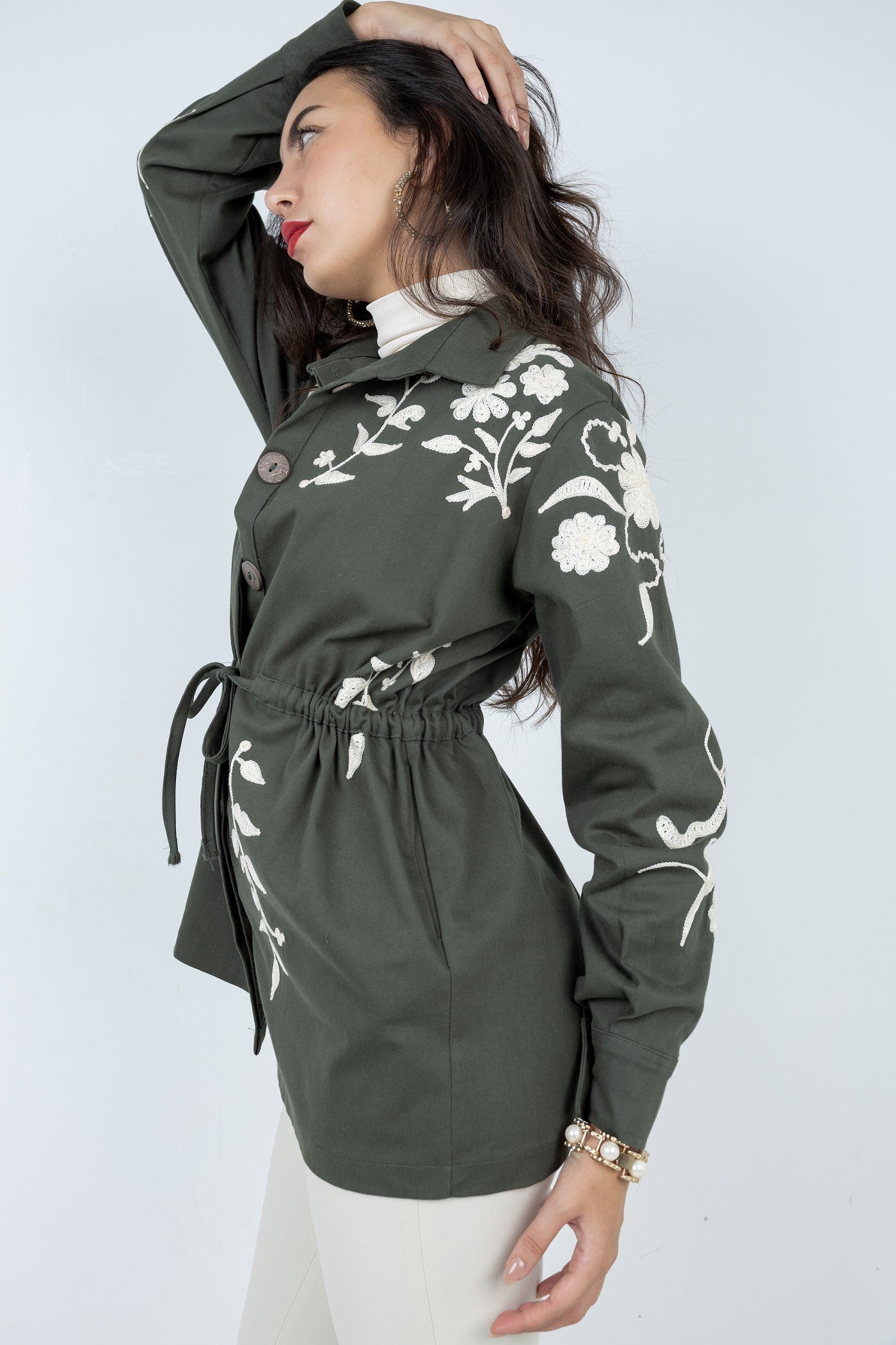 Woman wearing a green jacket with floral embroidery on a white background
