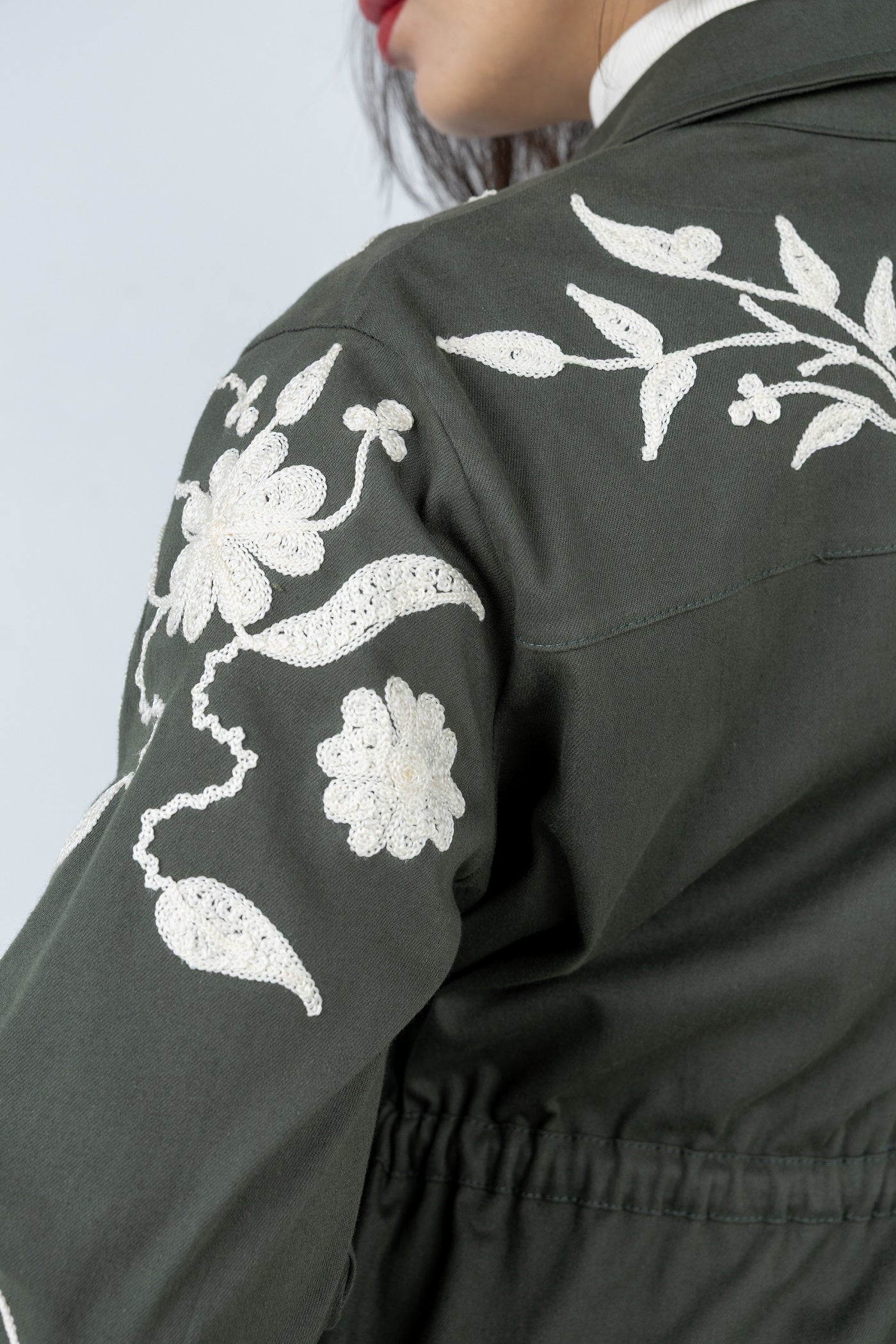 Dark green jacket with white floral embroidery on a light gray background