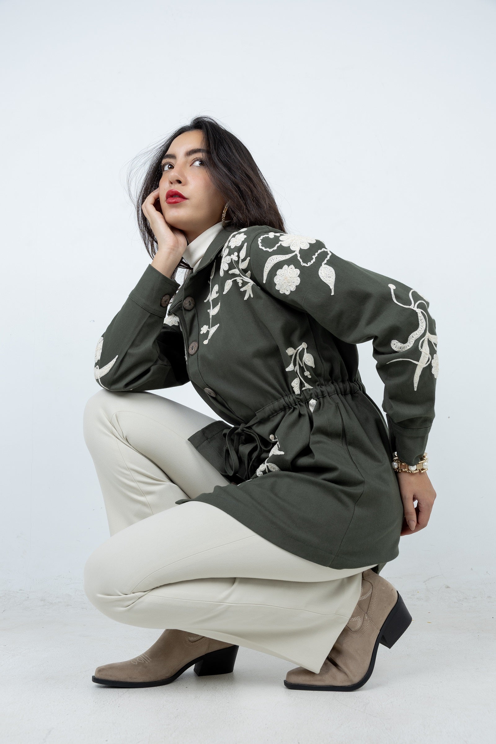 Woman wearing a green floral embroidered jacket on a white background