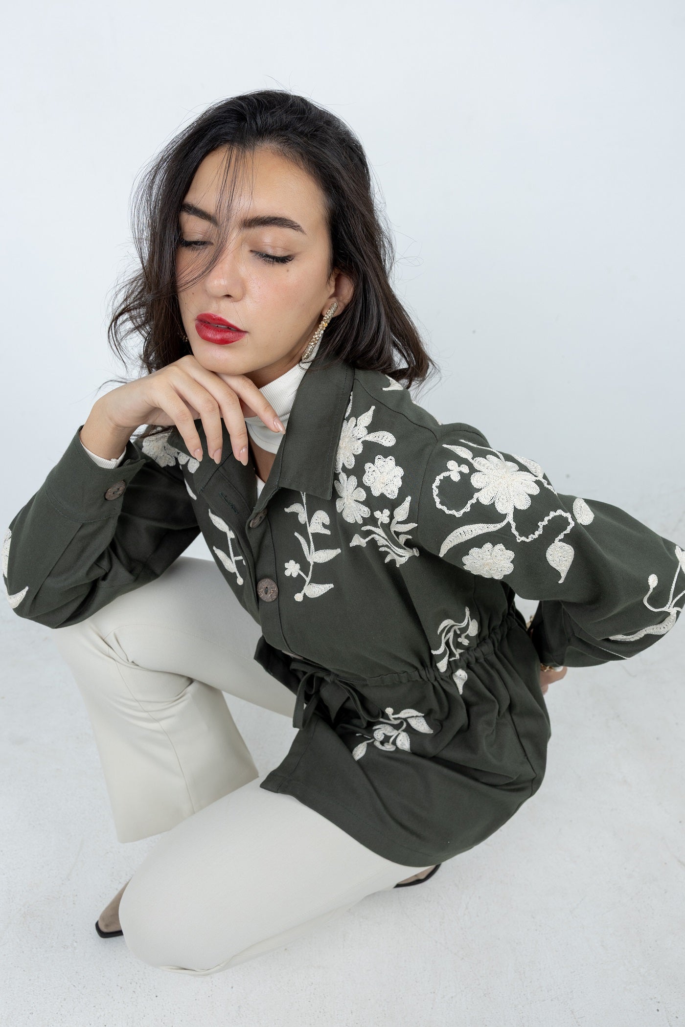 Woman wearing a green jacket with white floral patterns on a white background