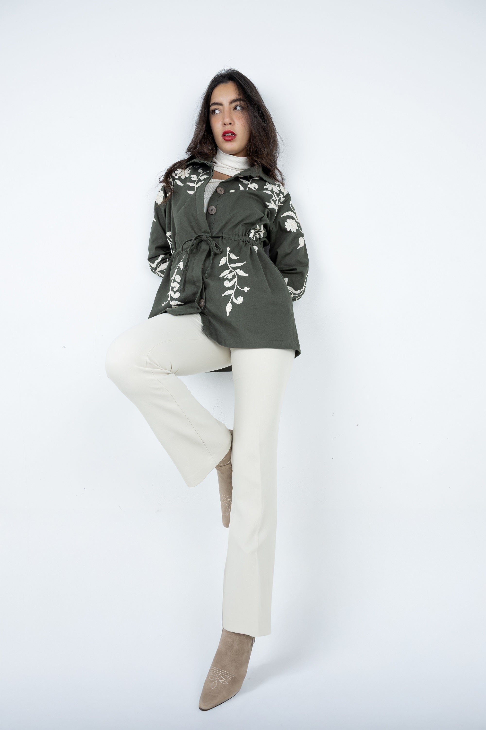 Woman wearing a green floral-patterned coat with white pants on a white background