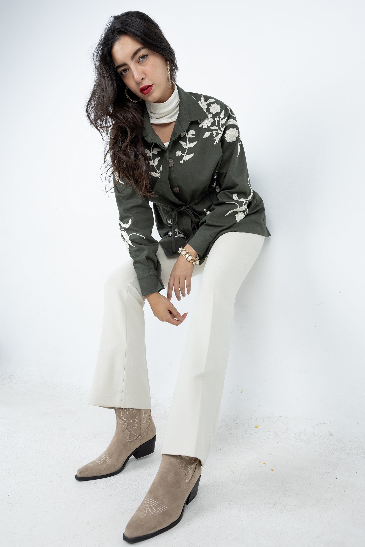 Woman wearing a green floral blouse, white pants, and brown boots on a white background