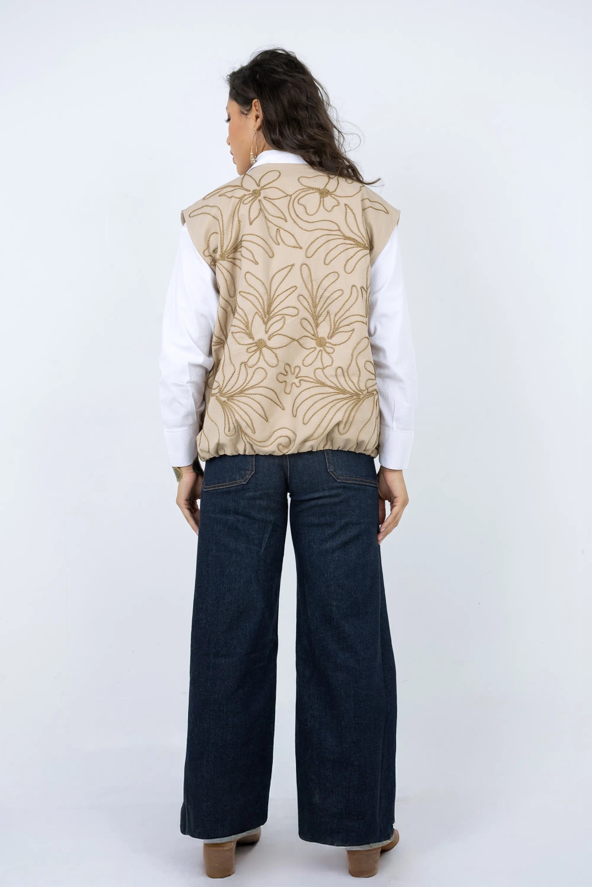 Person wearing a beige floral-patterned vest over a white shirt with dark blue pants on a white background