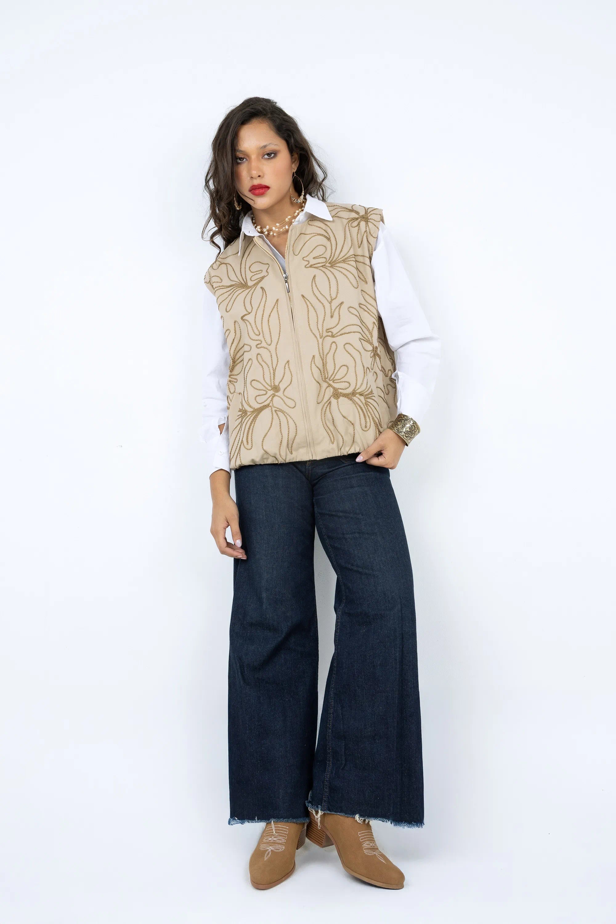 Woman wearing a patterned vest, white shirt, blue jeans, and brown boots on a white background