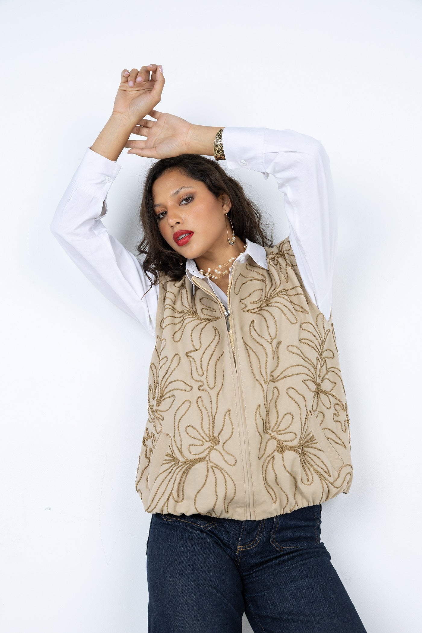 Woman wearing a beige floral-patterned top with a white shirt underneath on a white background