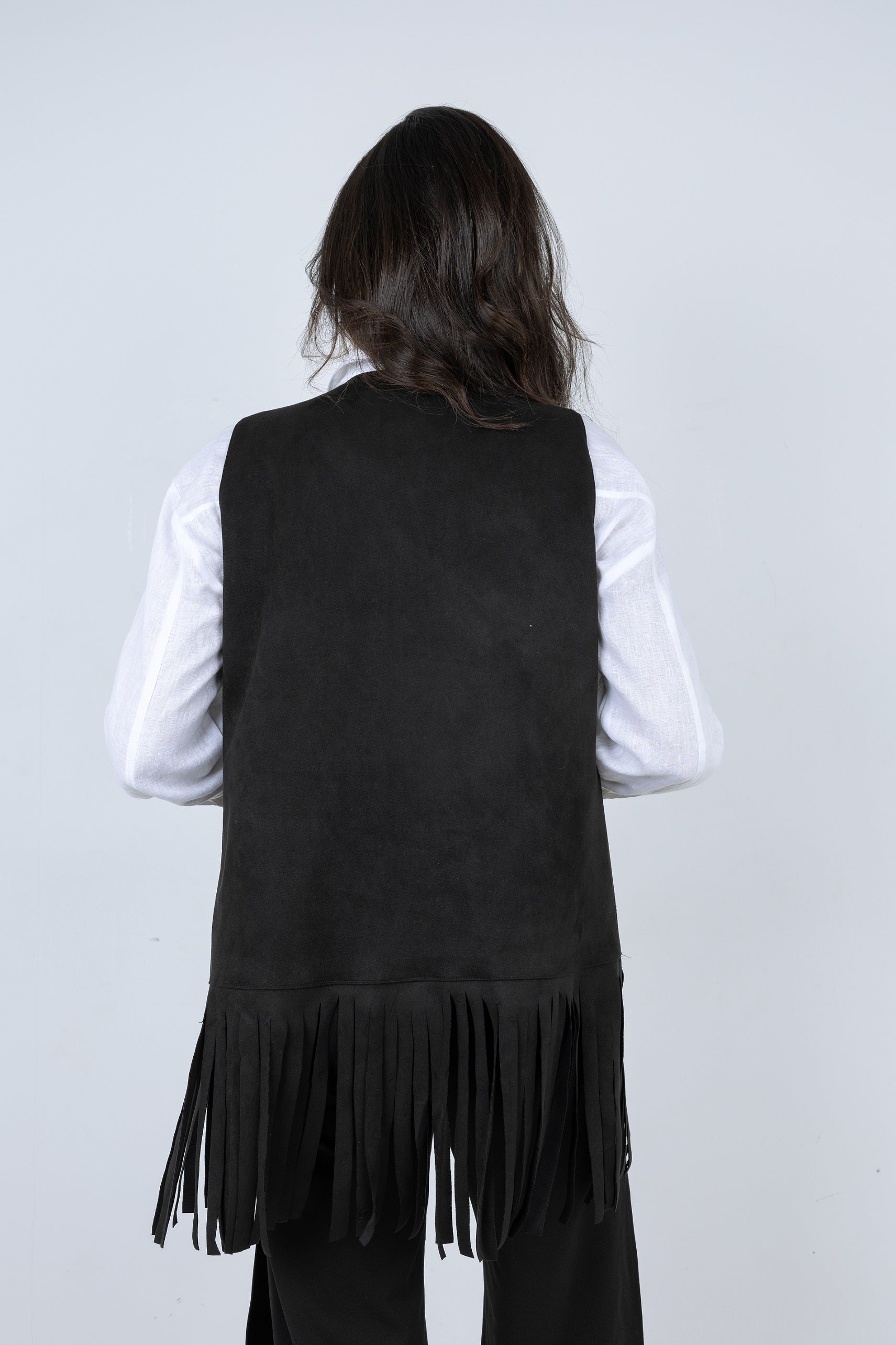 Person wearing a black fringed vest over a white shirt on a light gray background