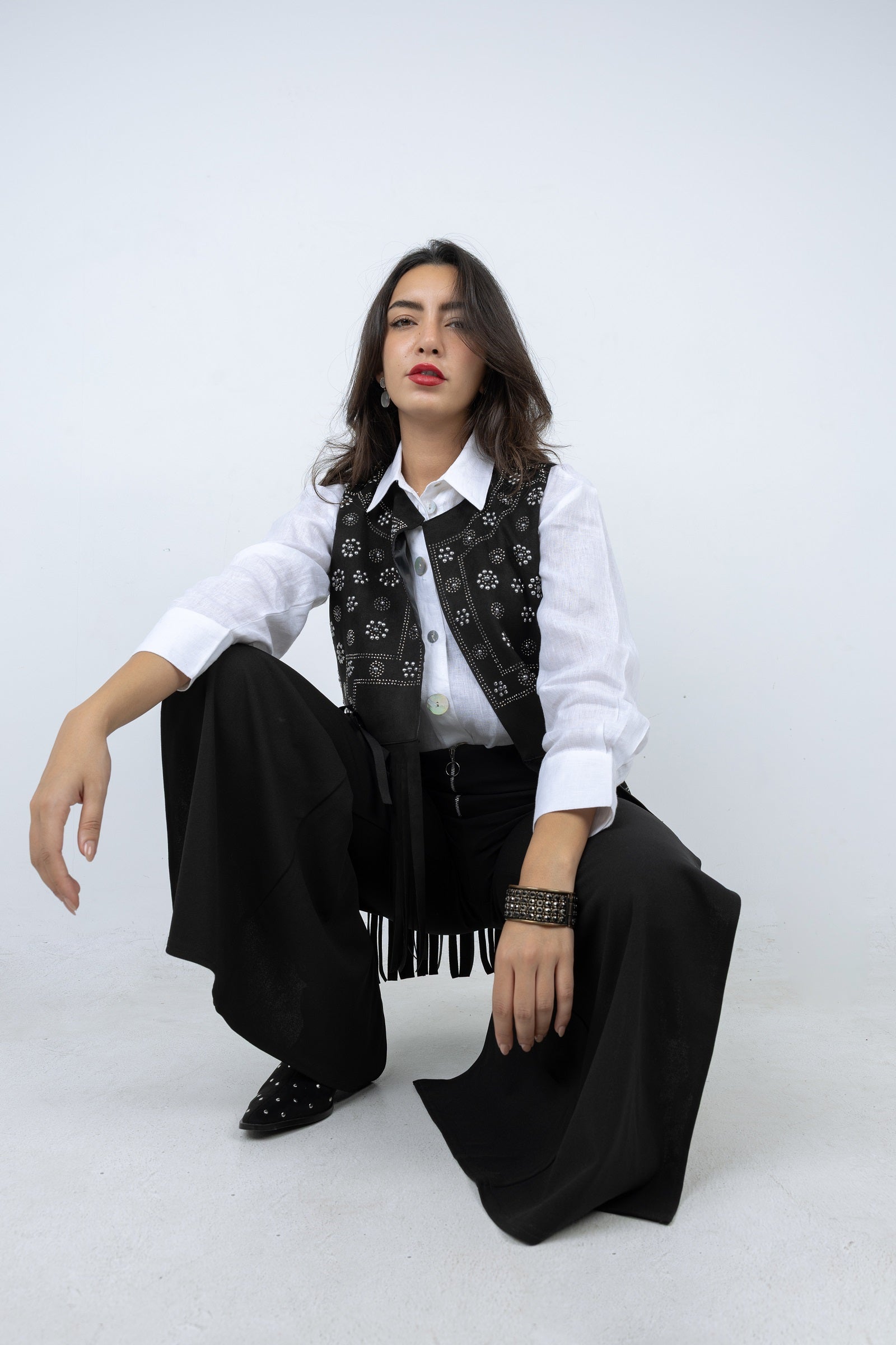 Woman wearing a white shirt, black vest, and black pants sitting on a white background