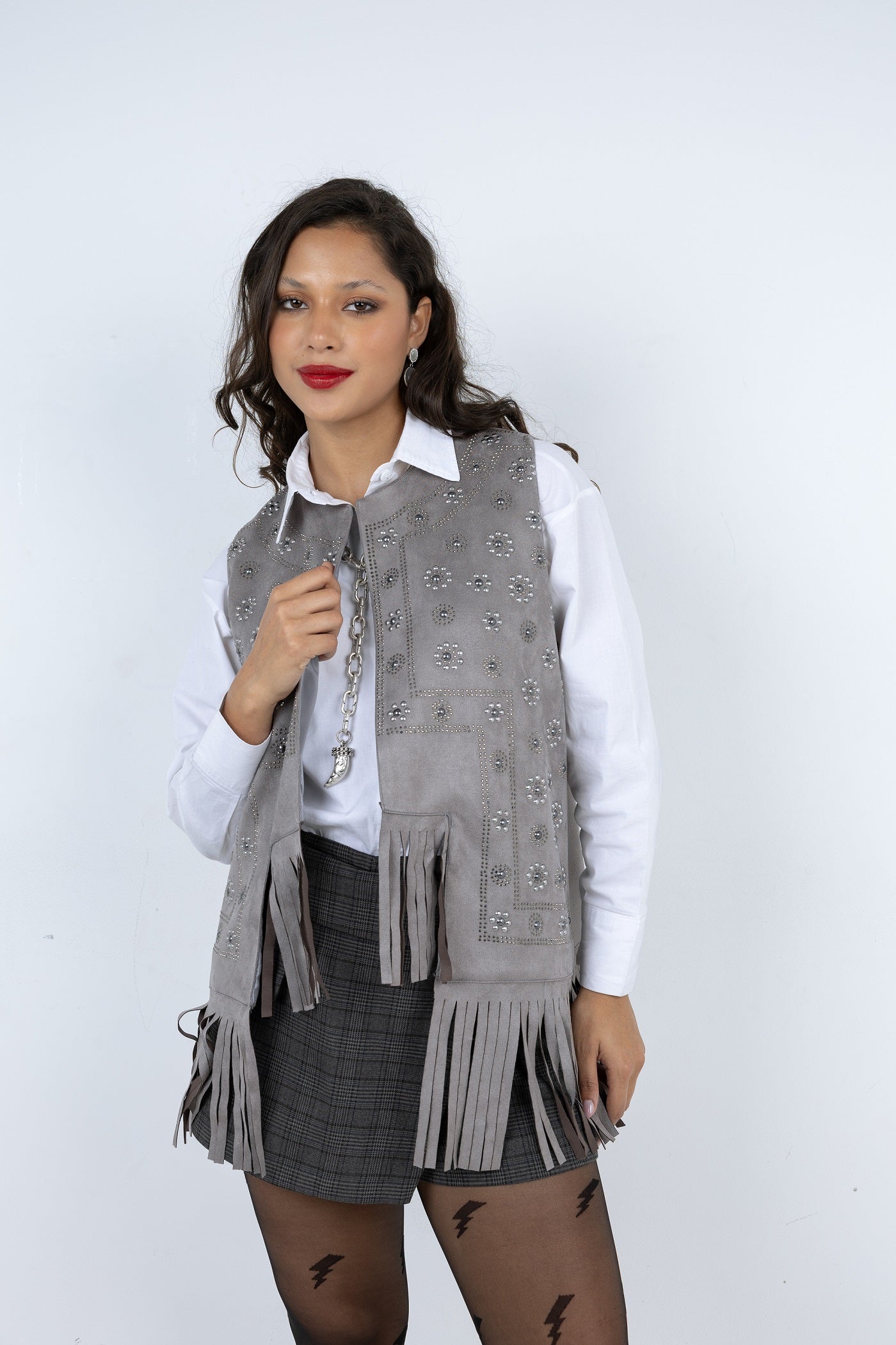 Woman wearing a gray fringed vest over a white shirt on a white background
