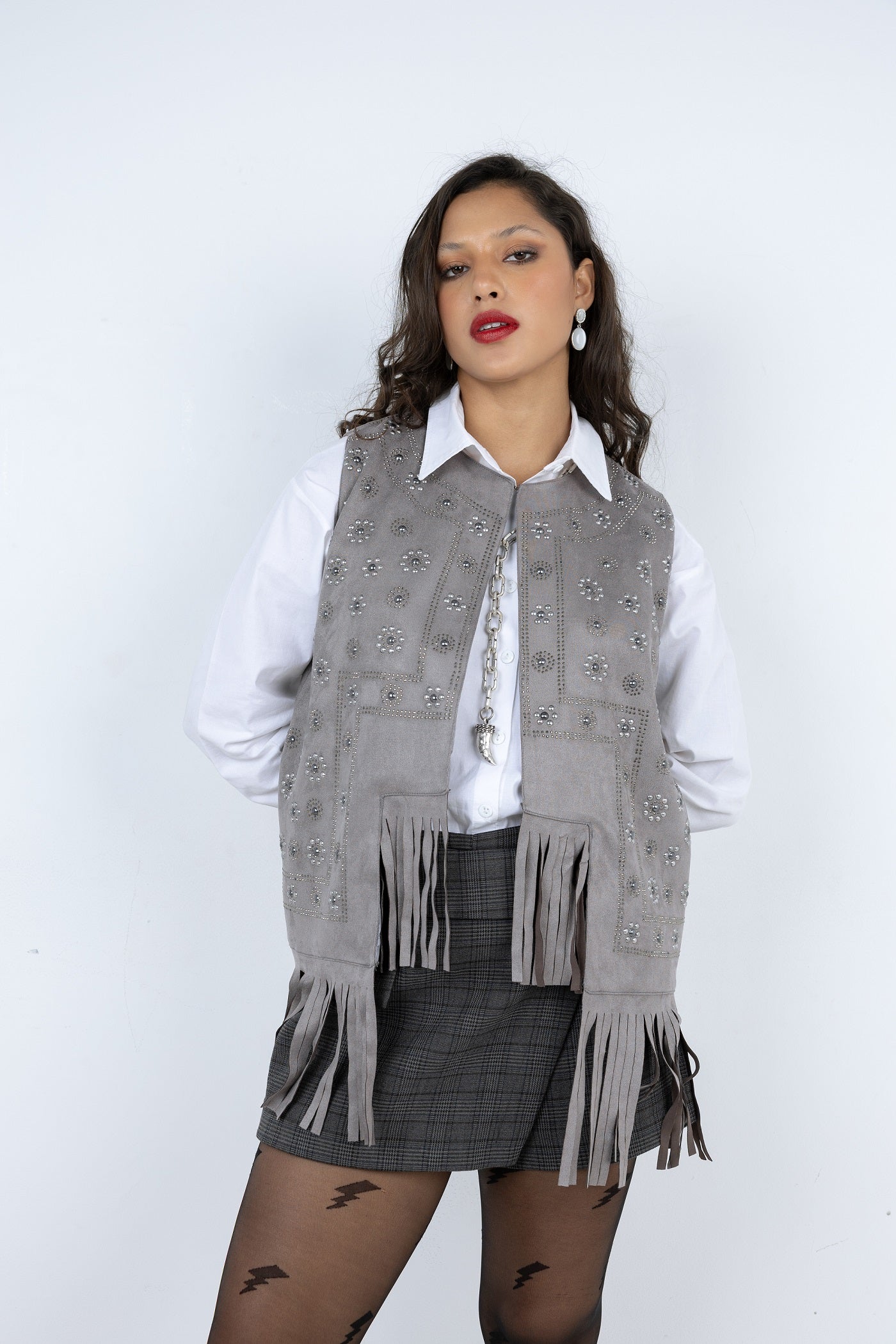 Woman wearing a gray patterned vest with fringes on a white background