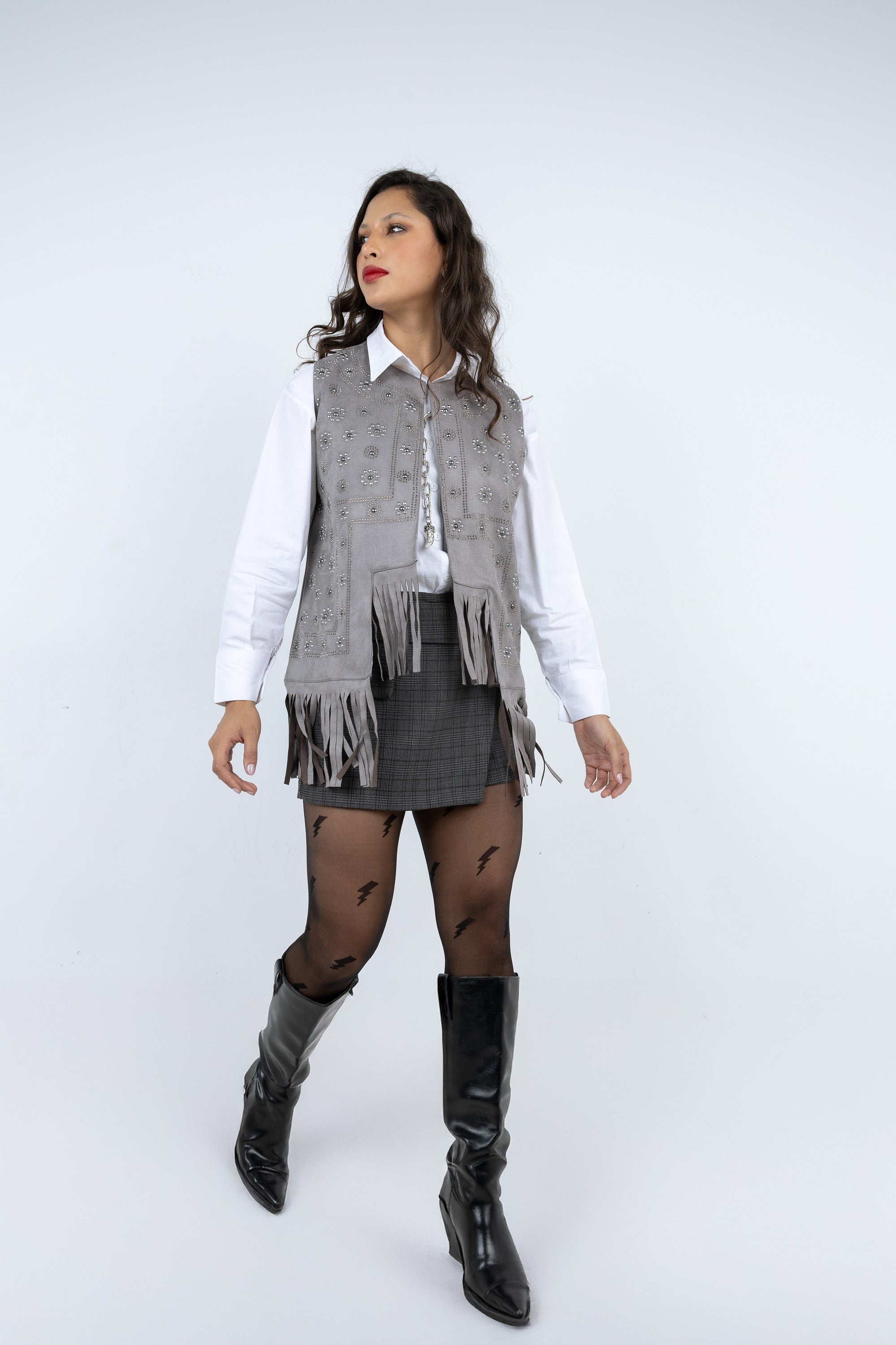 Woman wearing a white shirt, gray vest with fringes, gray skirt, and black knee-high boots on a white background