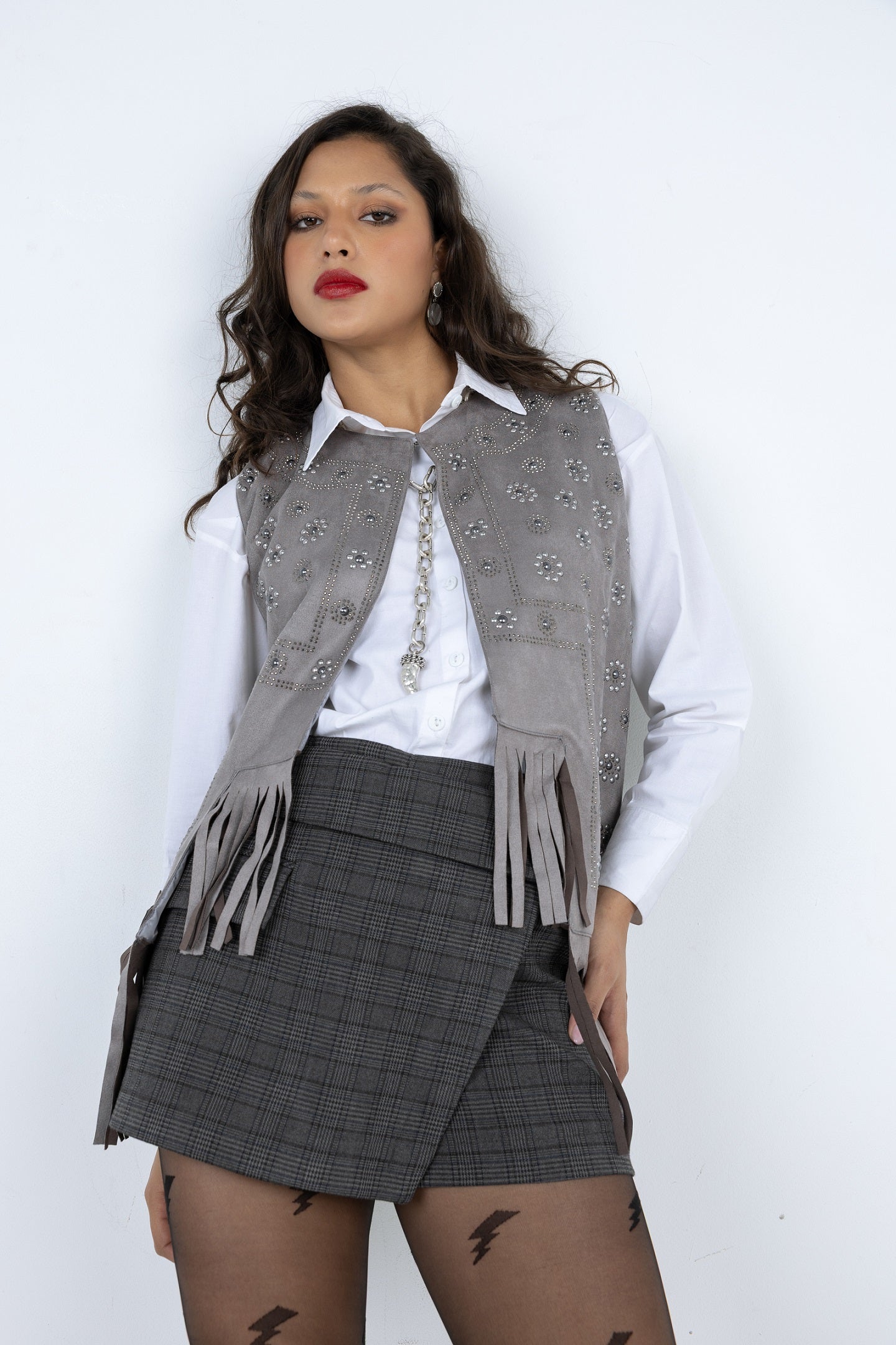 Woman wearing a gray patterned vest over a white shirt with a gray plaid skirt on a white background