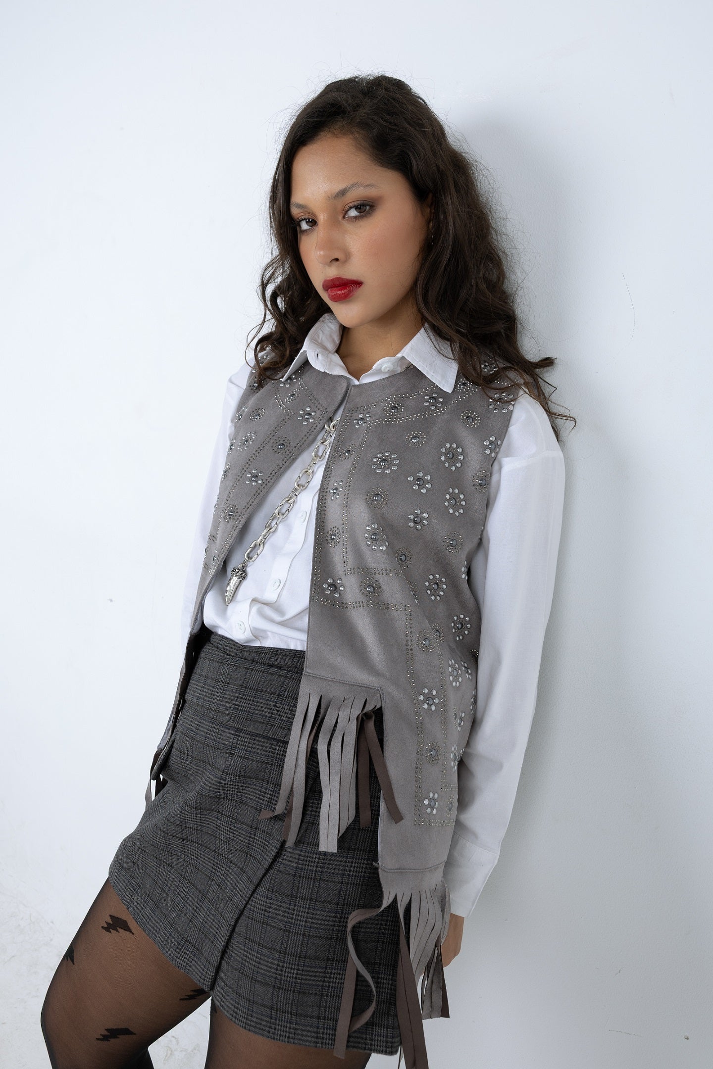 Woman wearing a gray vest with fringe and a white shirt against a white background