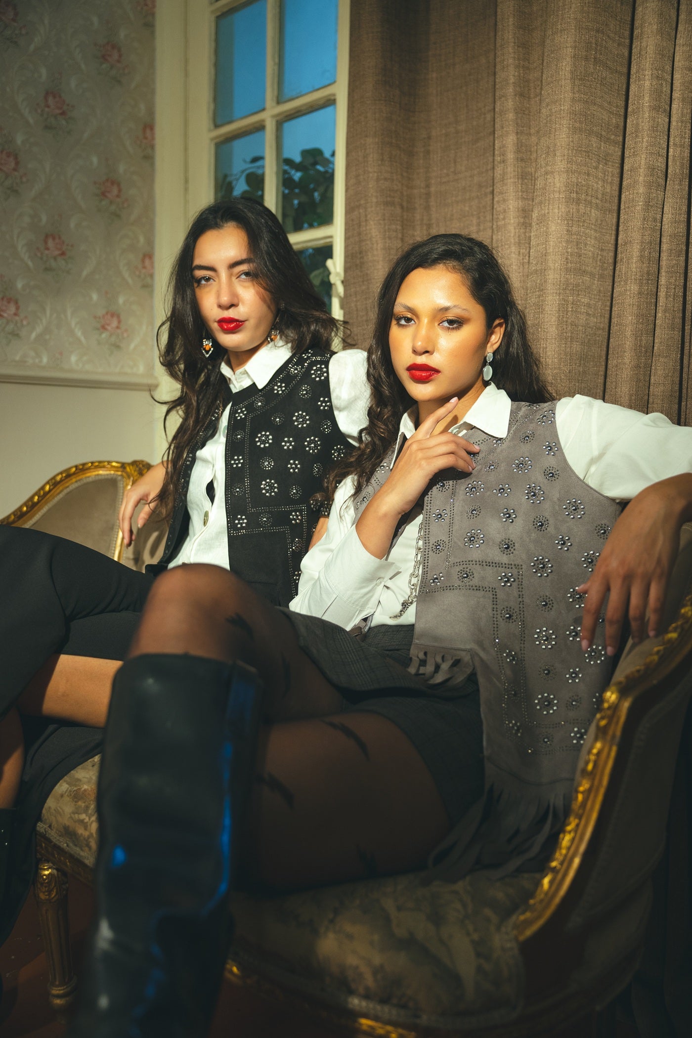 Two women sitting on a couch in an elegant room with floral wallpaper.