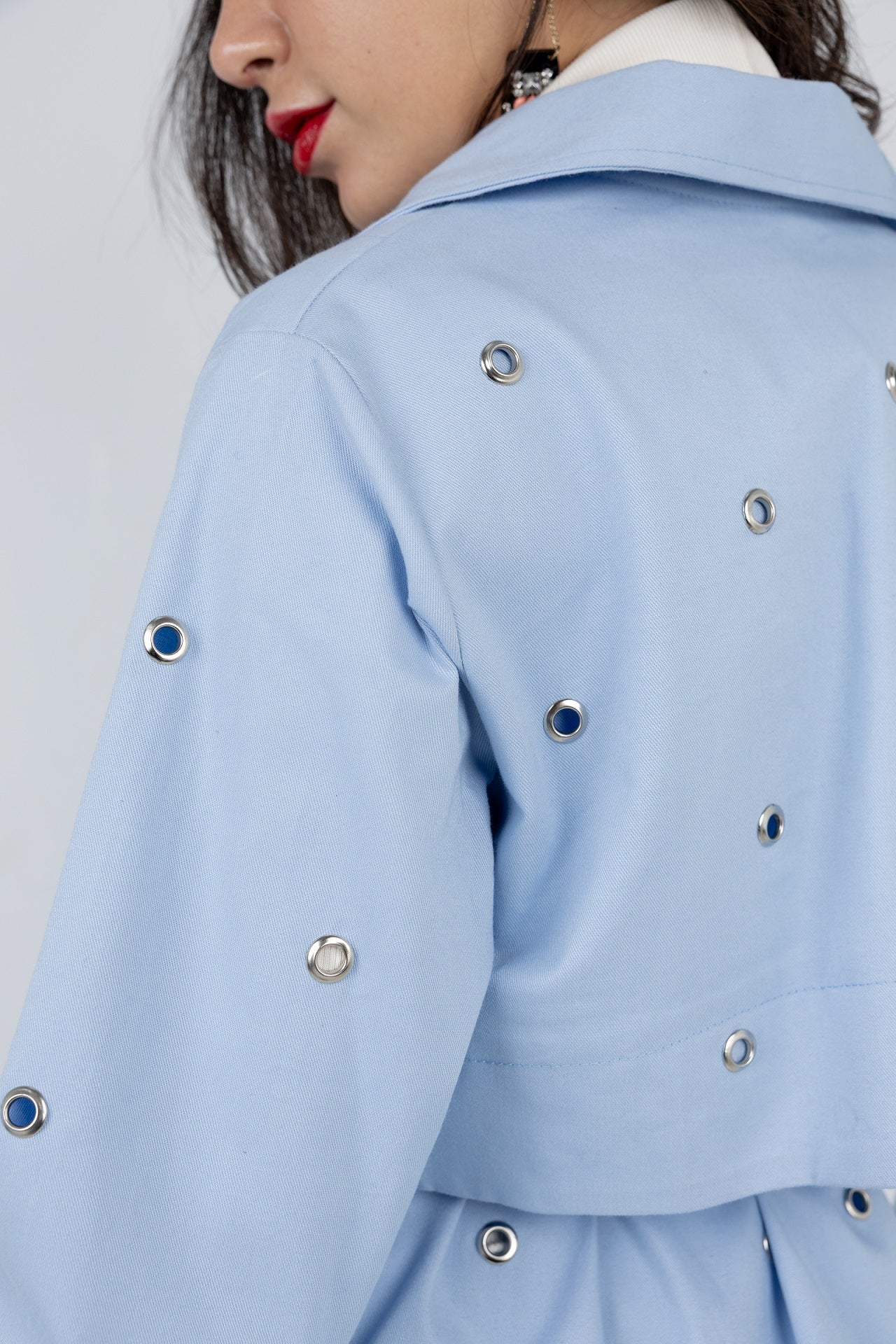 Close-up of a light blue coat with decorative buttons on a plain background