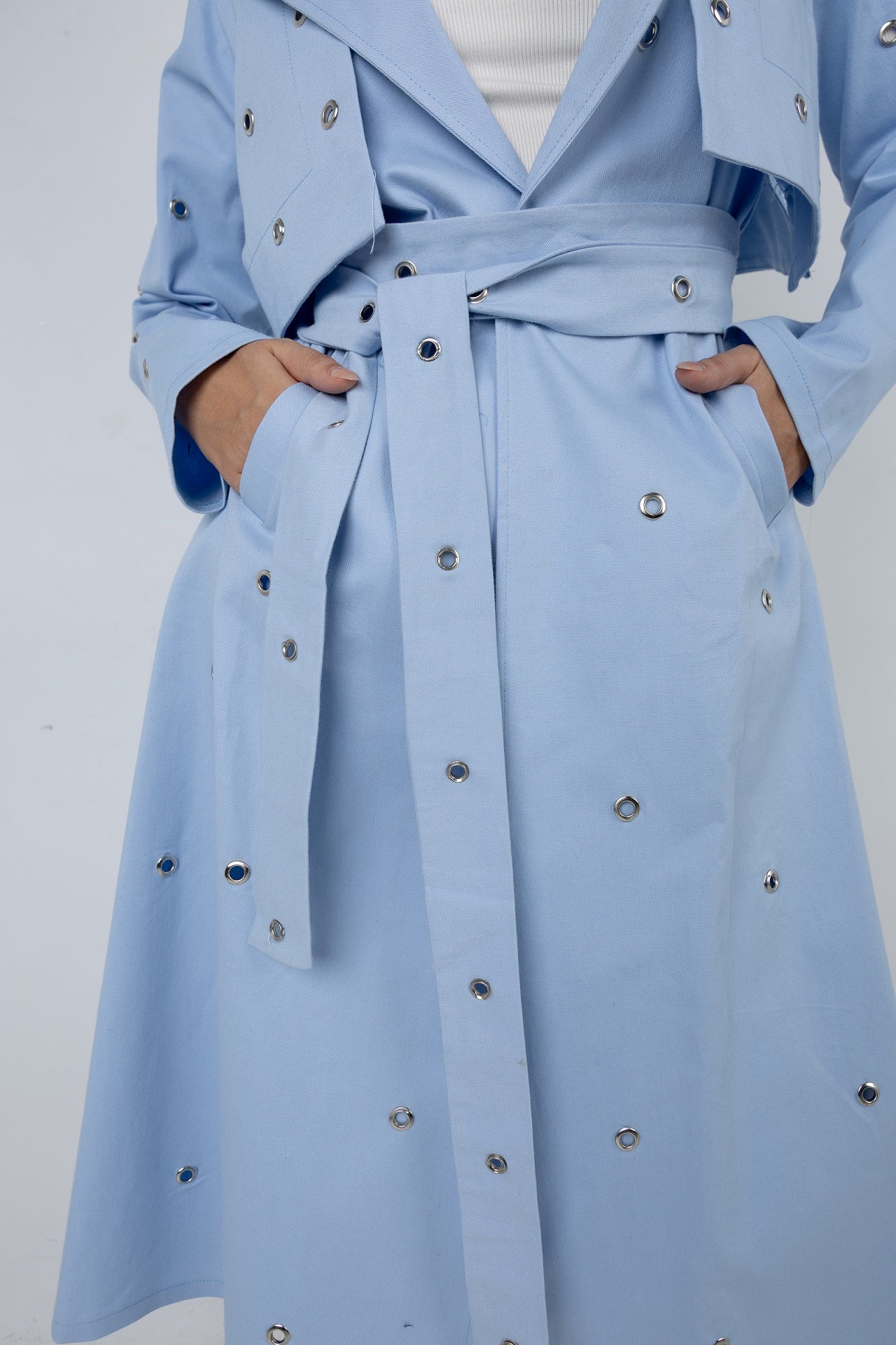 Light blue trench coat with decorative buttons on a white background