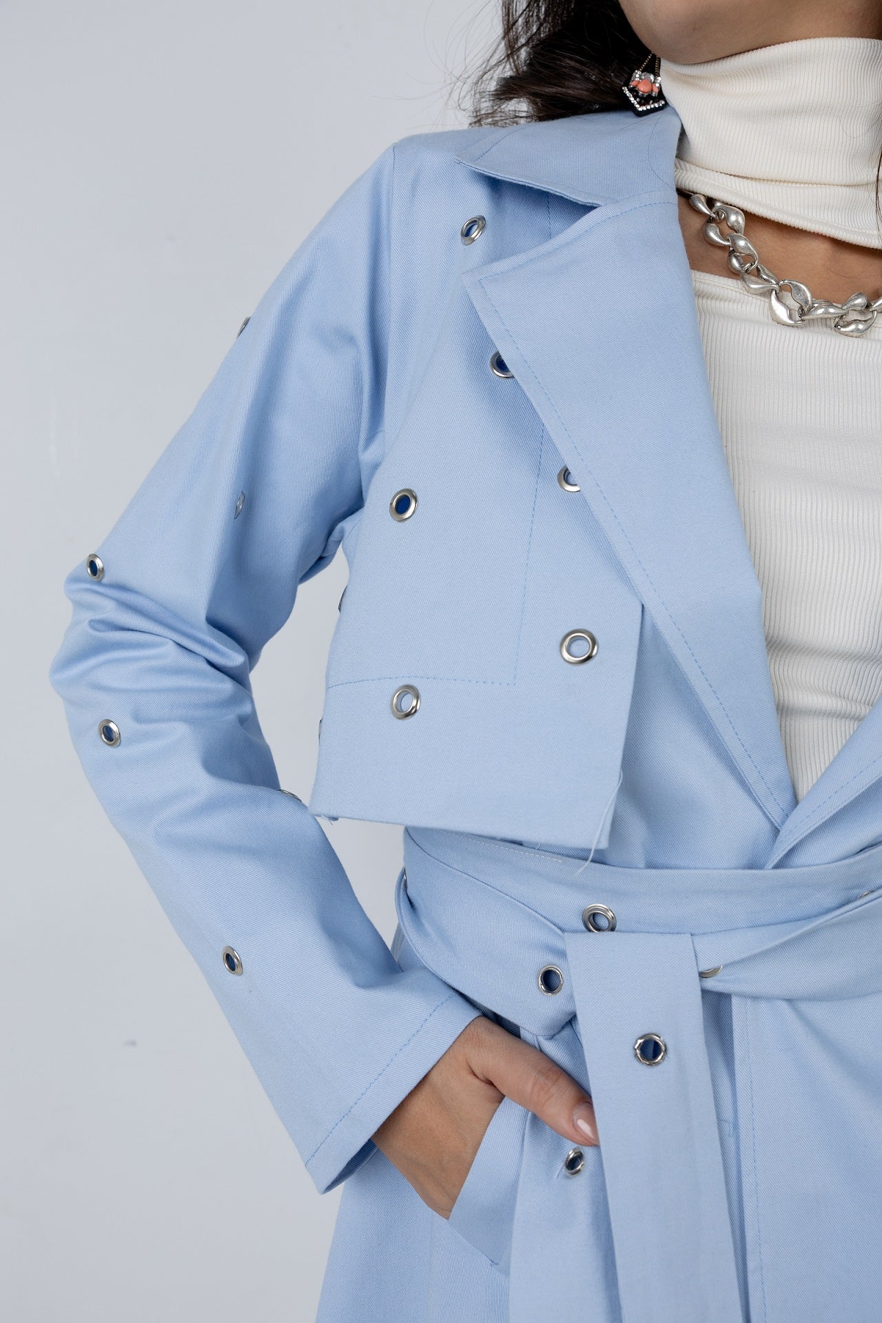 Light blue trench coat with silver buttons on a plain background