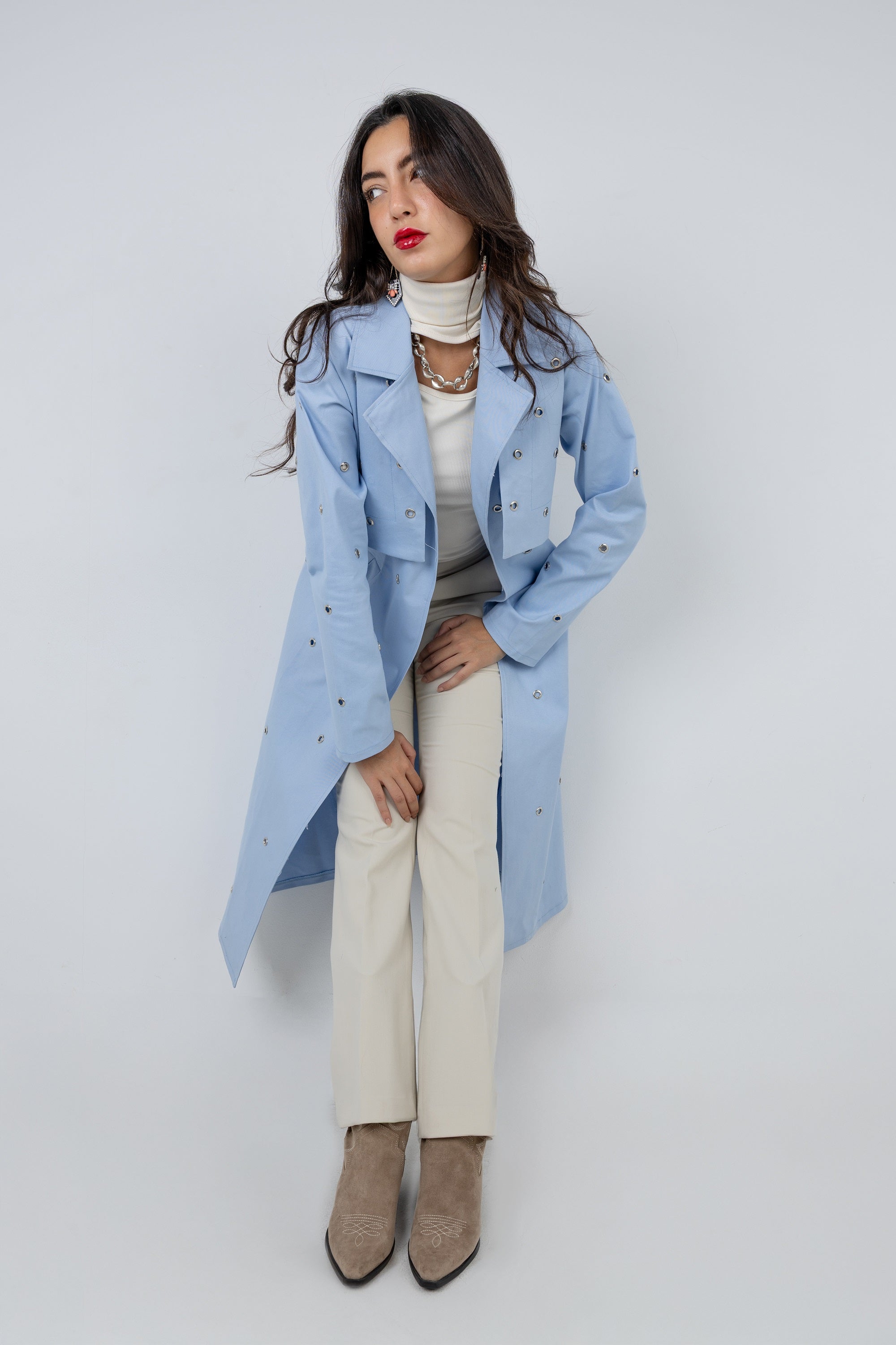 Woman wearing a light blue coat over a neutral outfit on a white background