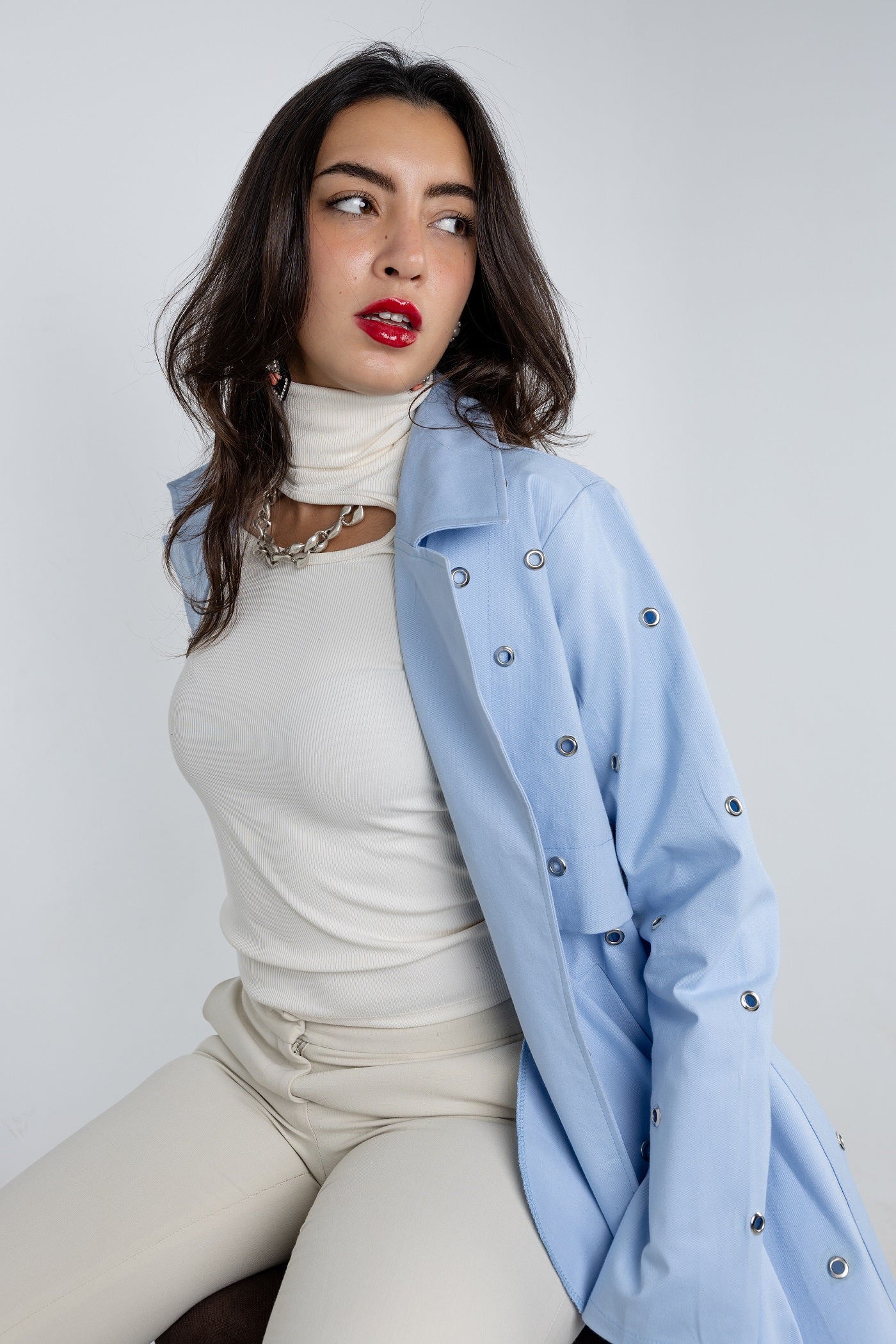 Woman wearing a light blue jacket over a white outfit on a plain background