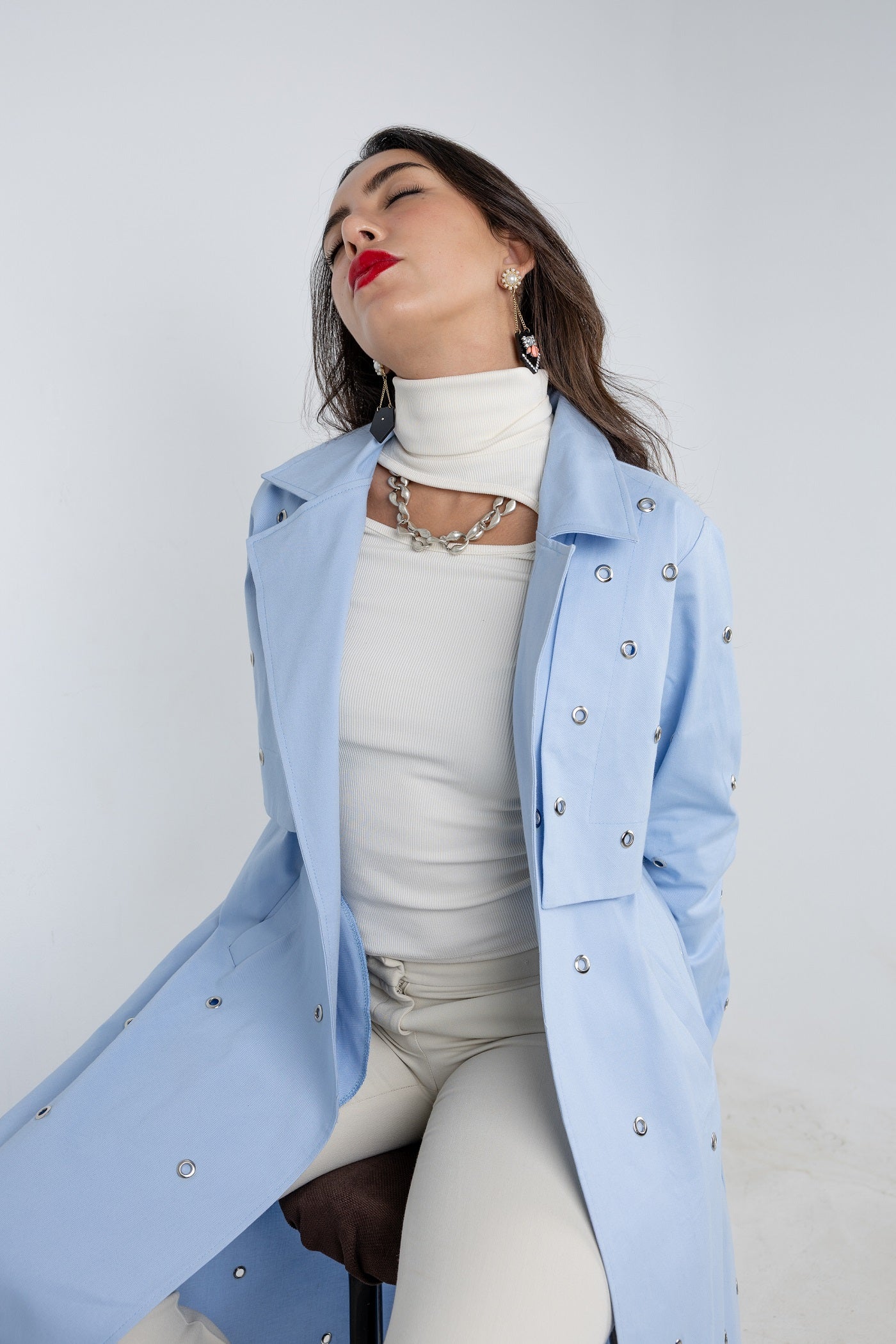 Woman wearing a light blue coat with a white outfit against a plain background