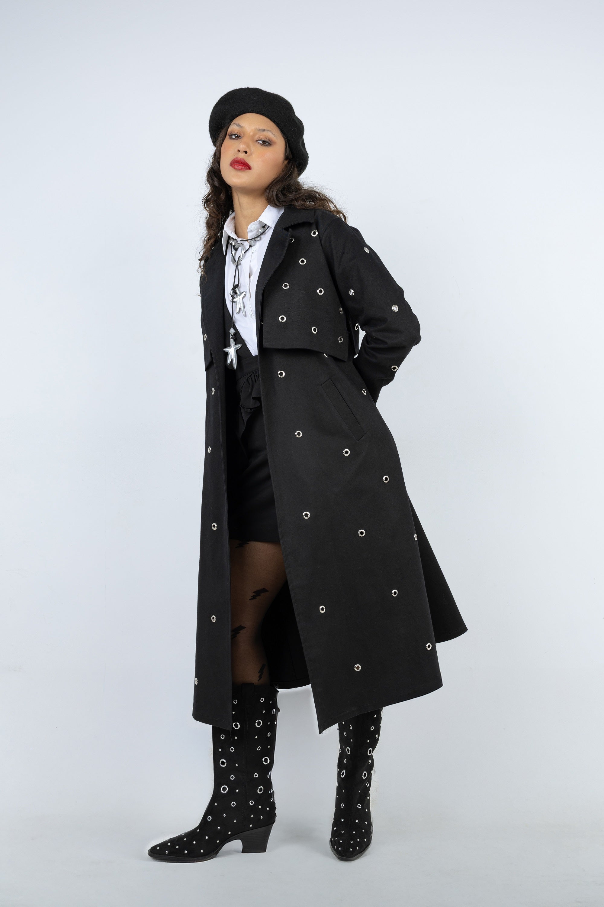 Woman wearing a long black coat with silver buttons on a white background