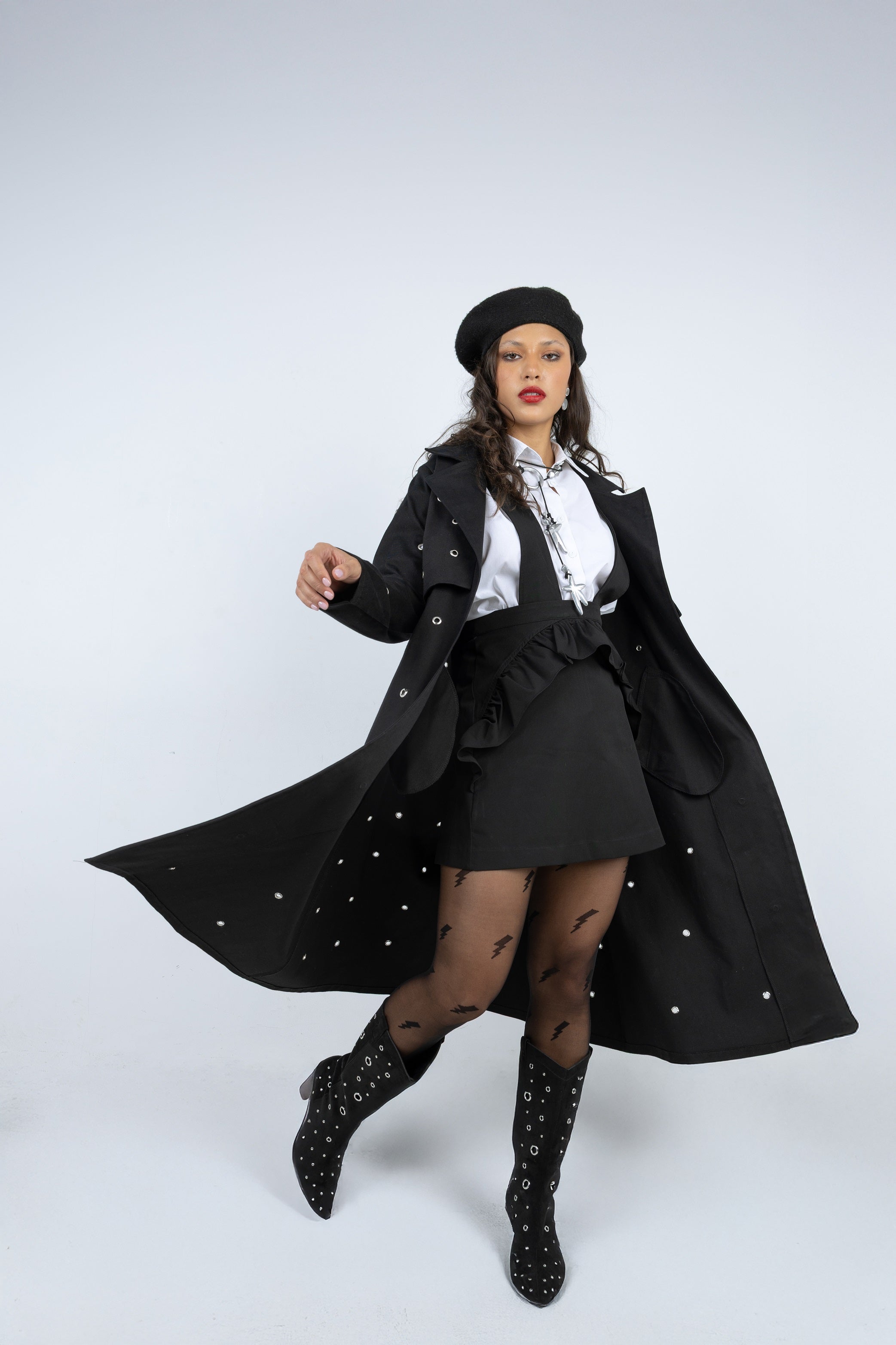 Woman in a black coat, skirt, and boots with a white shirt underneath on a white background