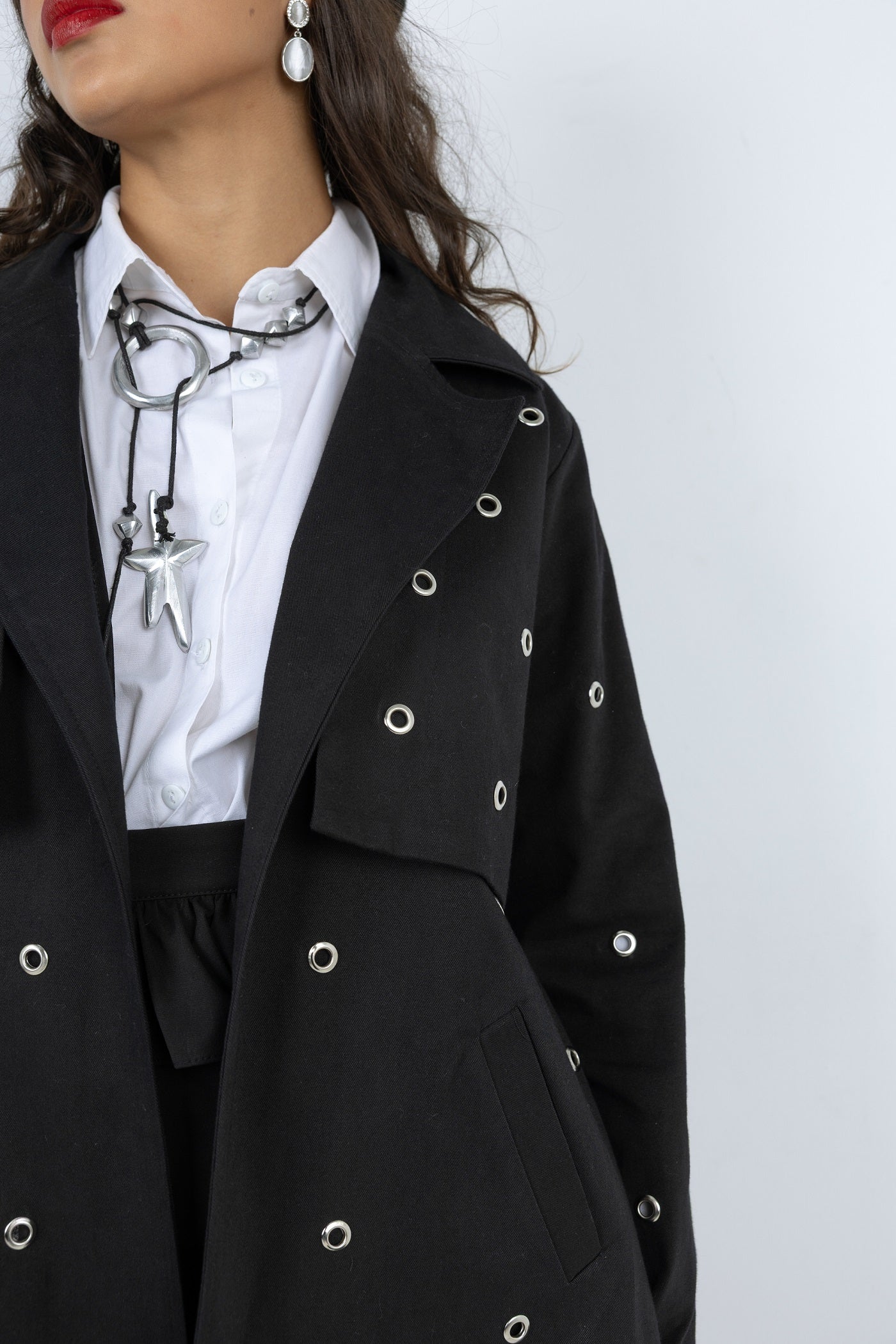 Person wearing a black coat with silver buttons on a white background