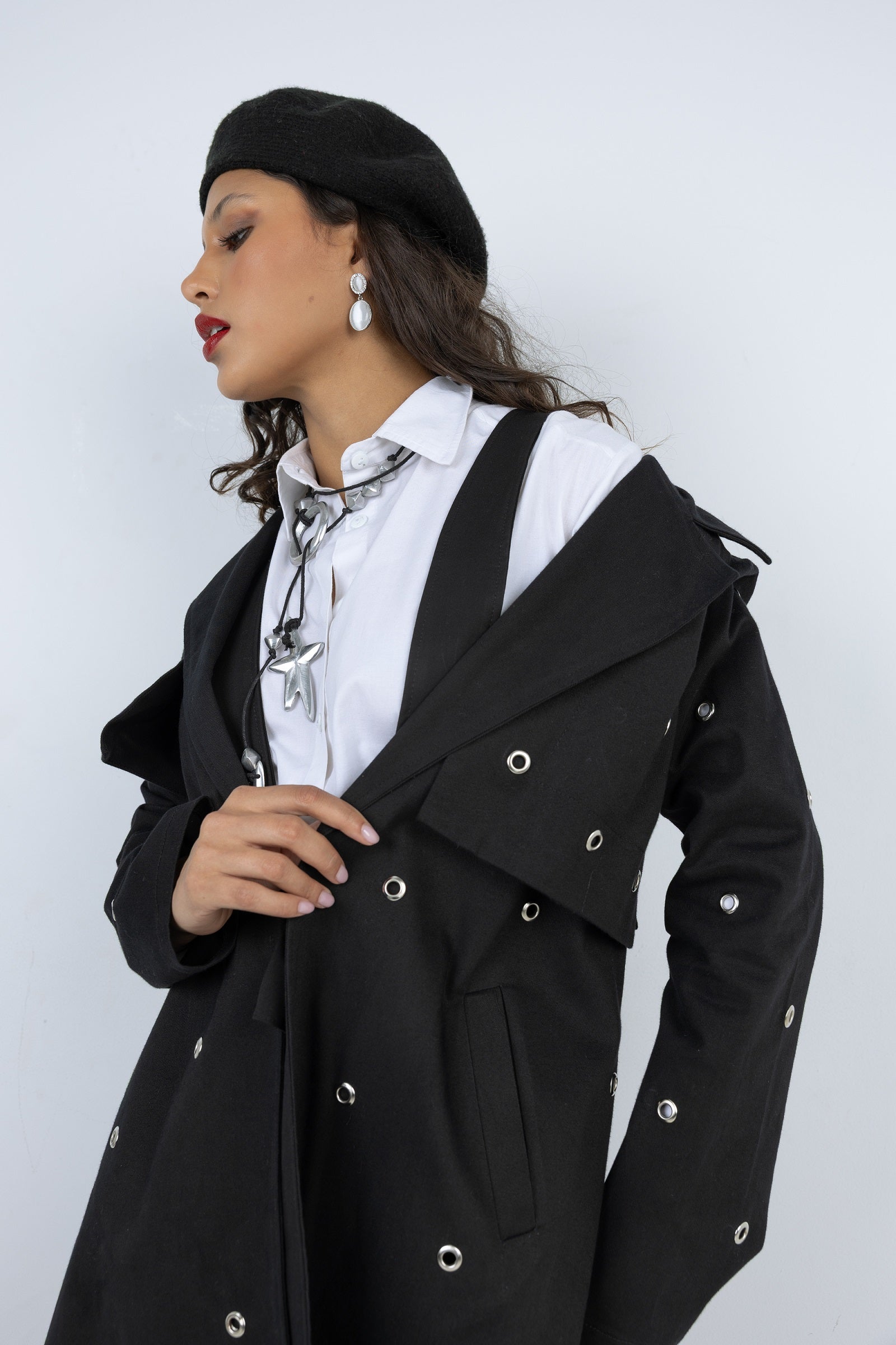 Woman wearing a black coat with silver buttons against a white background