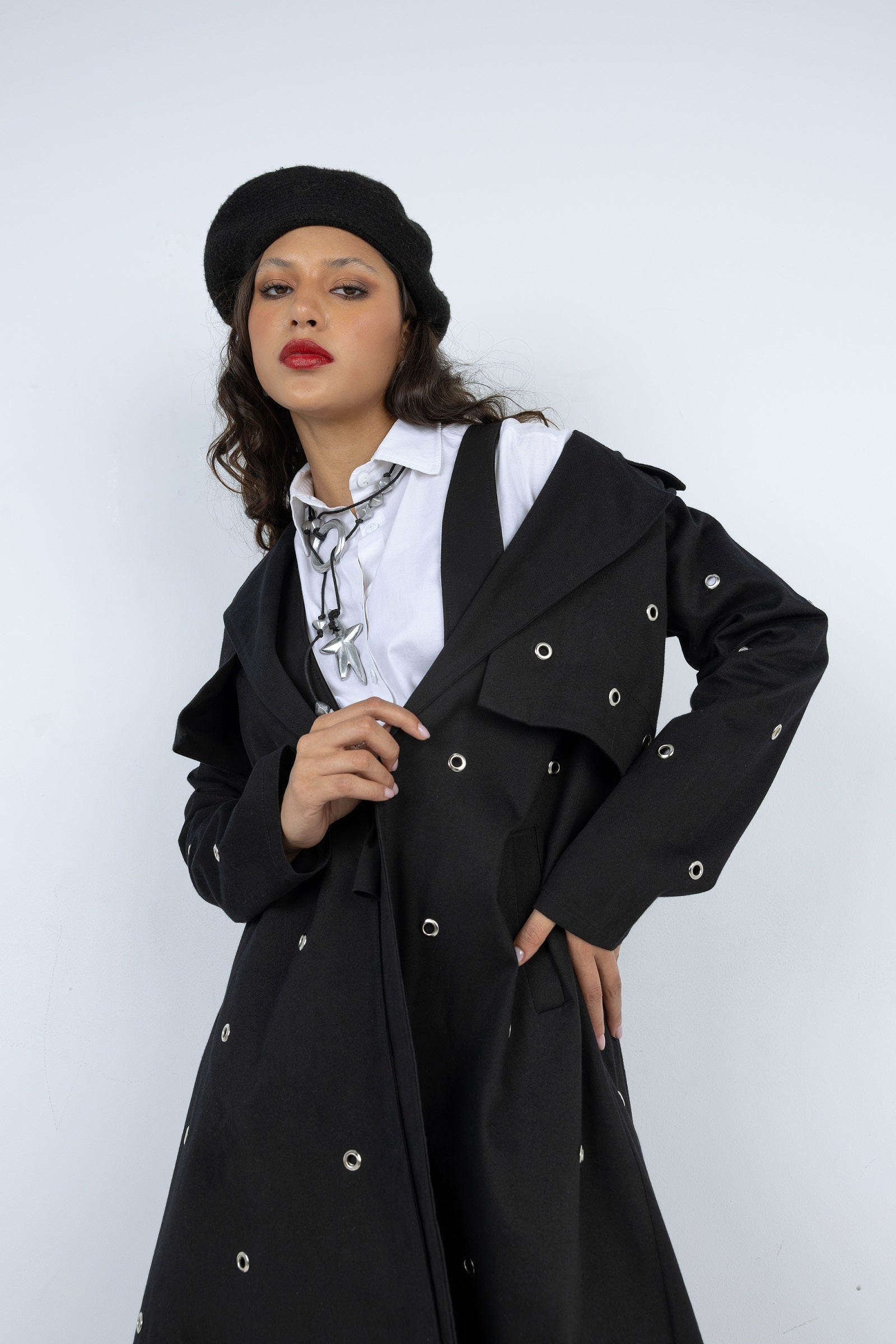 Woman wearing a black coat with silver buttons against a white background