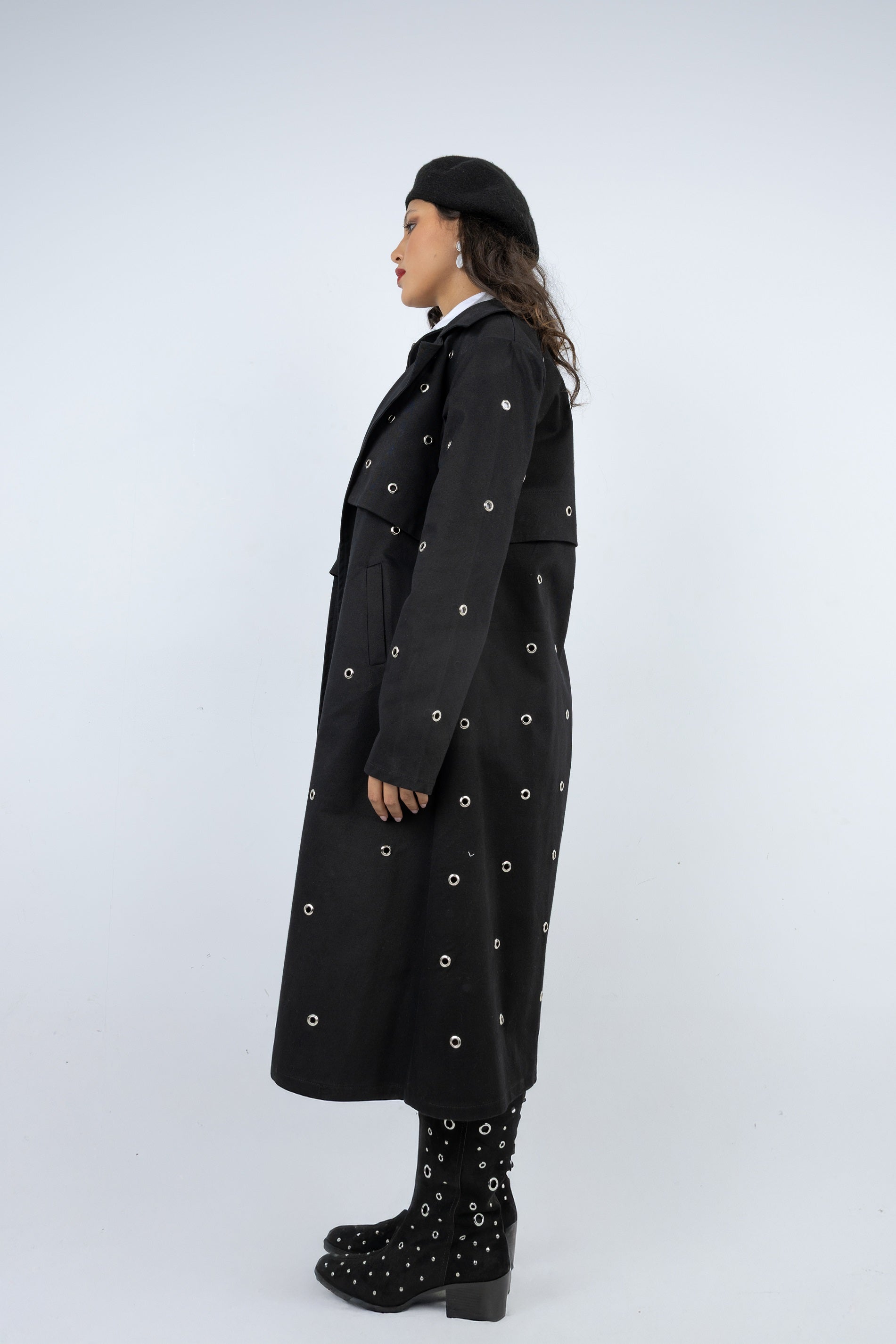 Person wearing a long black coat with decorative buttons on a white background