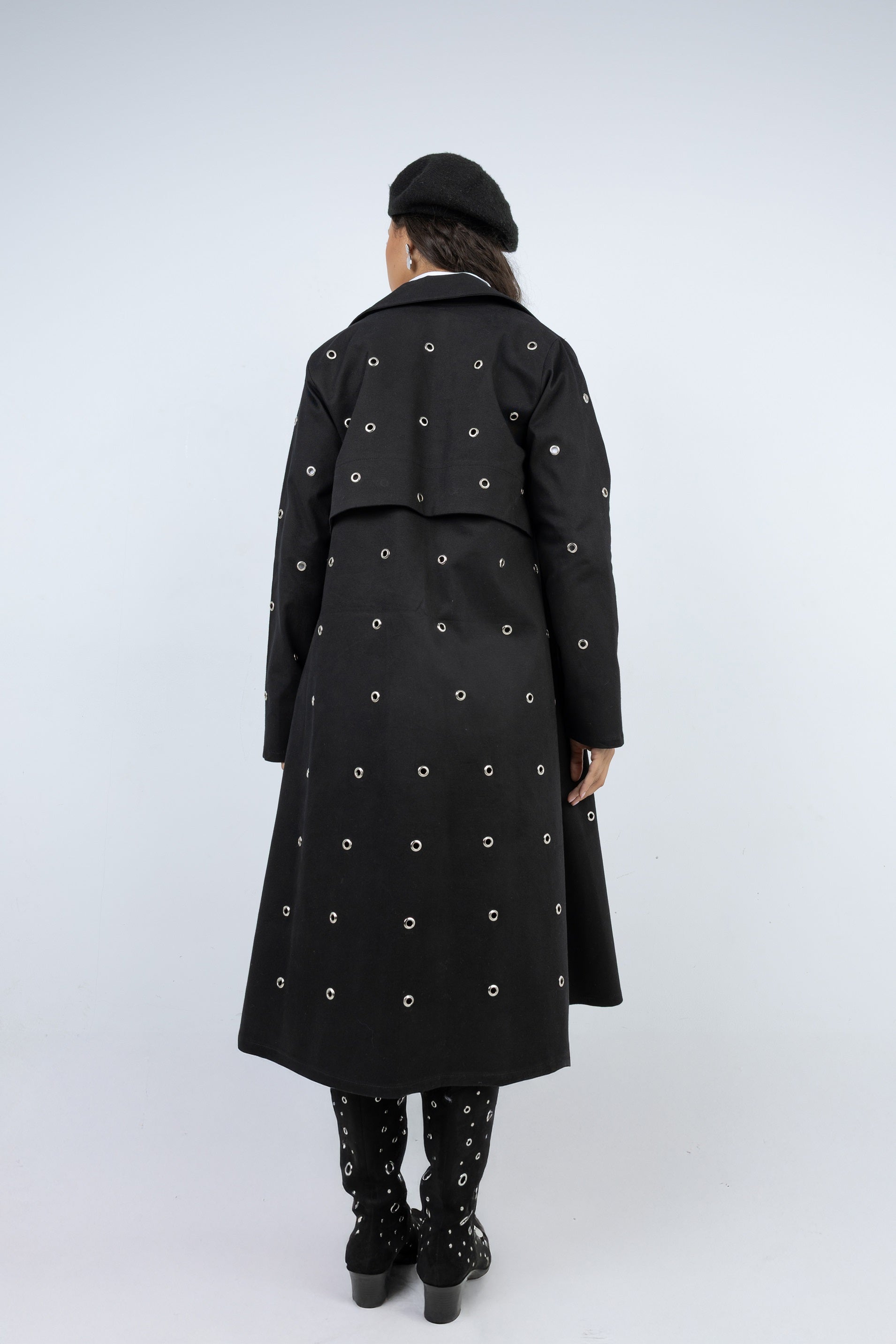 Person wearing a long black coat with white patterns on a white background