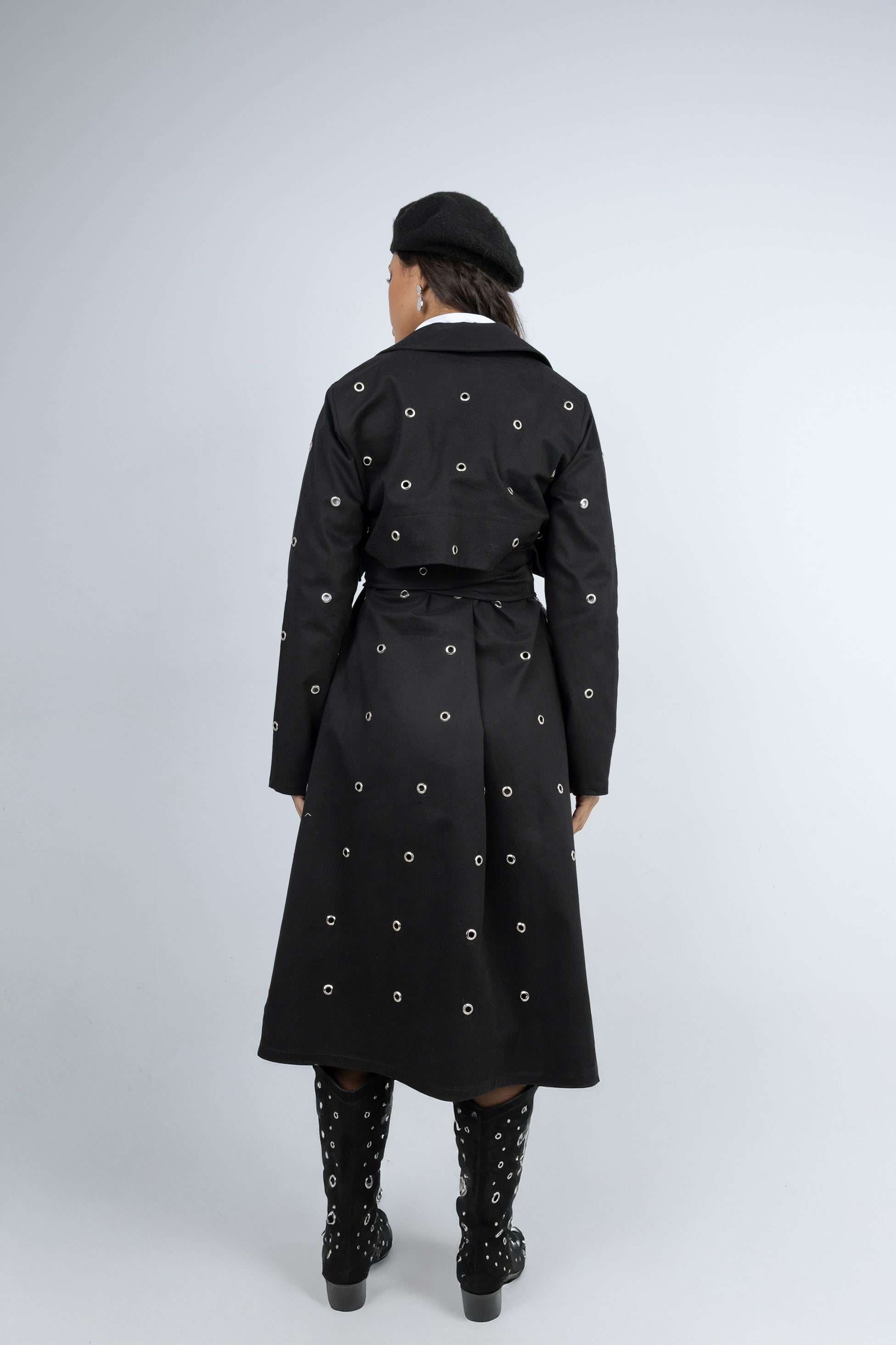 Person wearing a black trench coat with decorative buttons on a white background