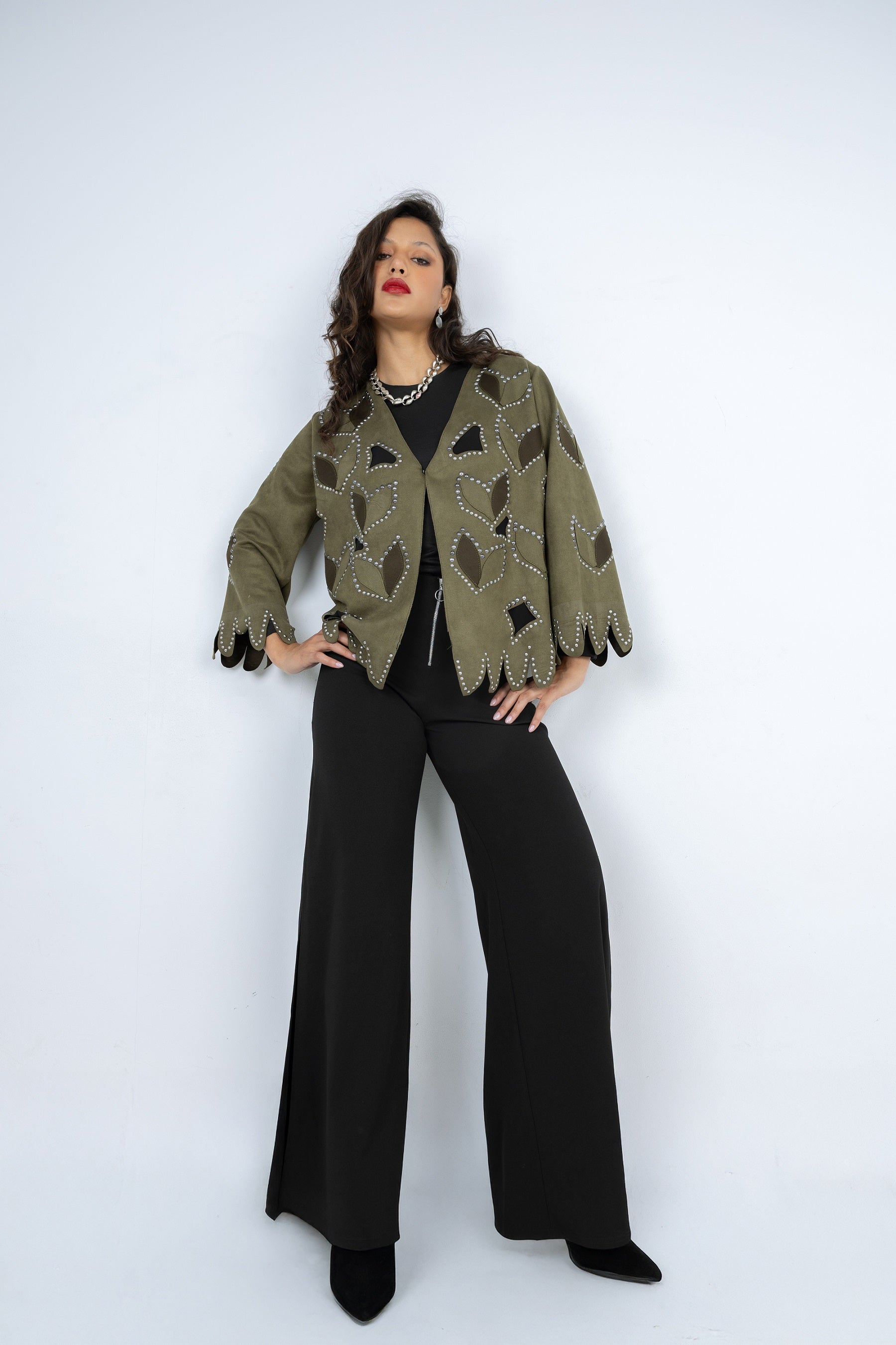 Woman wearing a patterned green jacket and black pants on a white background