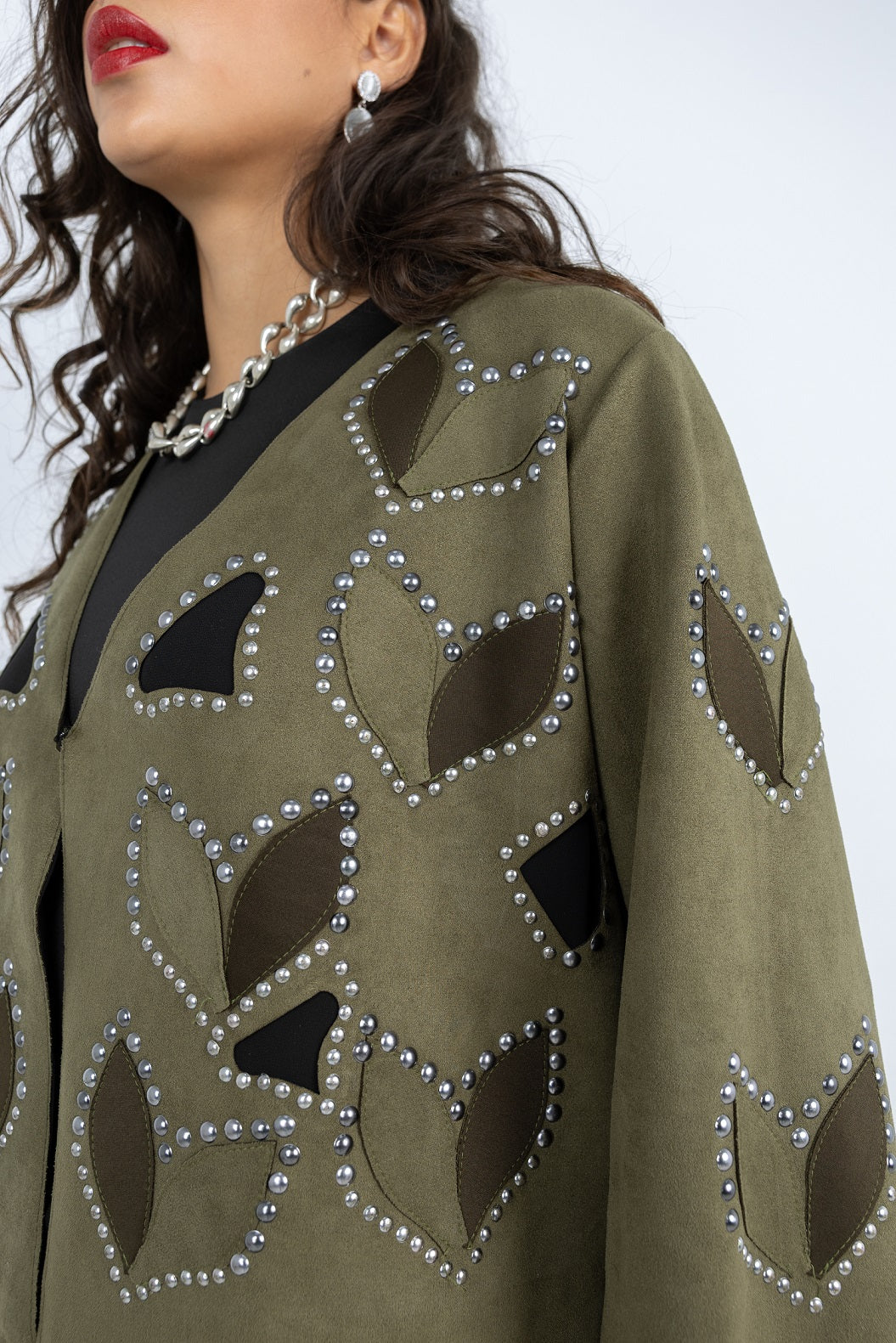 Close-up of a green garment with black and pearl embellishments on a white background