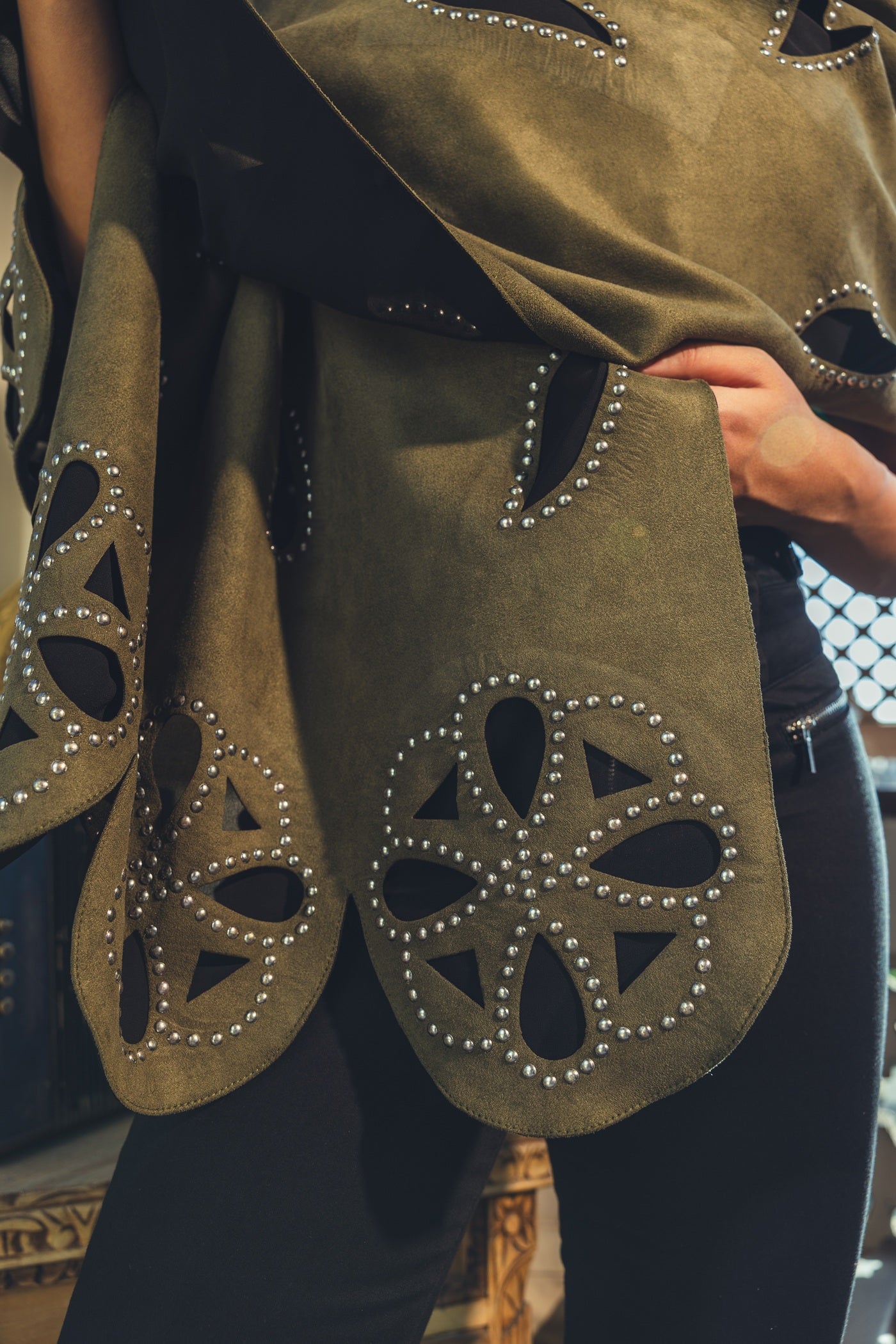 Green fabric with cut-out patterns and embellishments held by a person.