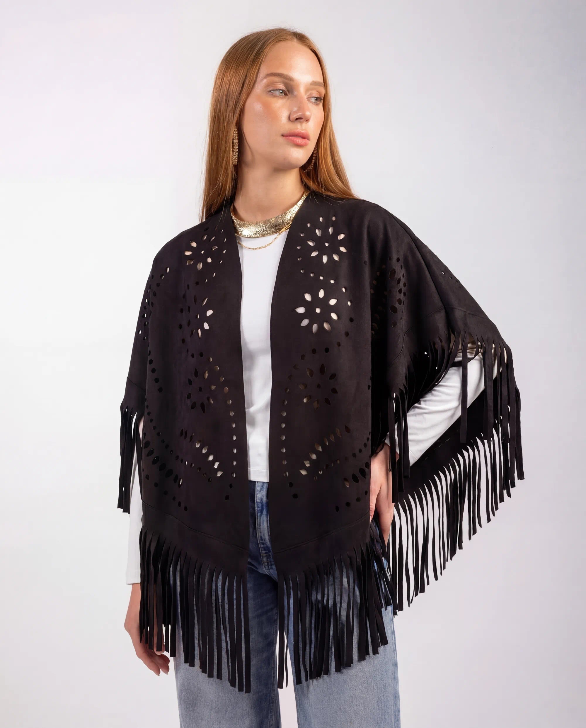 Woman wearing a black fringe poncho with cut-out patterns on a white background