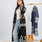Woman wearing a long black and white patterned cardigan with a plain background
