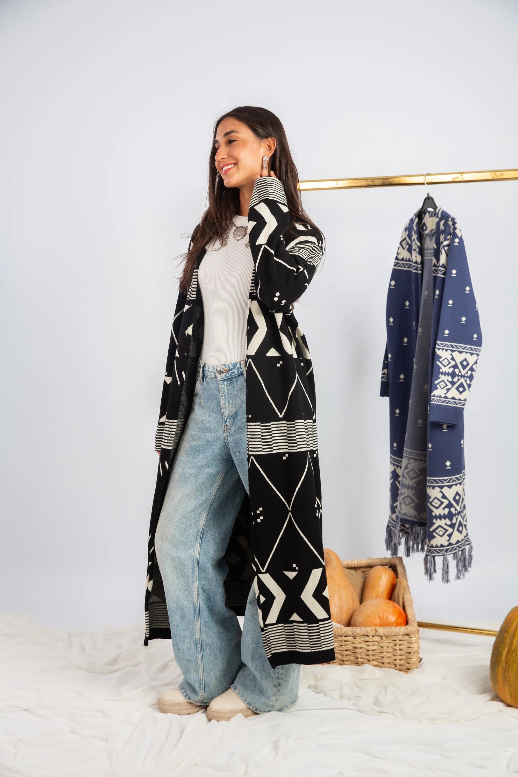 Woman wearing a long black and white patterned cardigan with a plain background