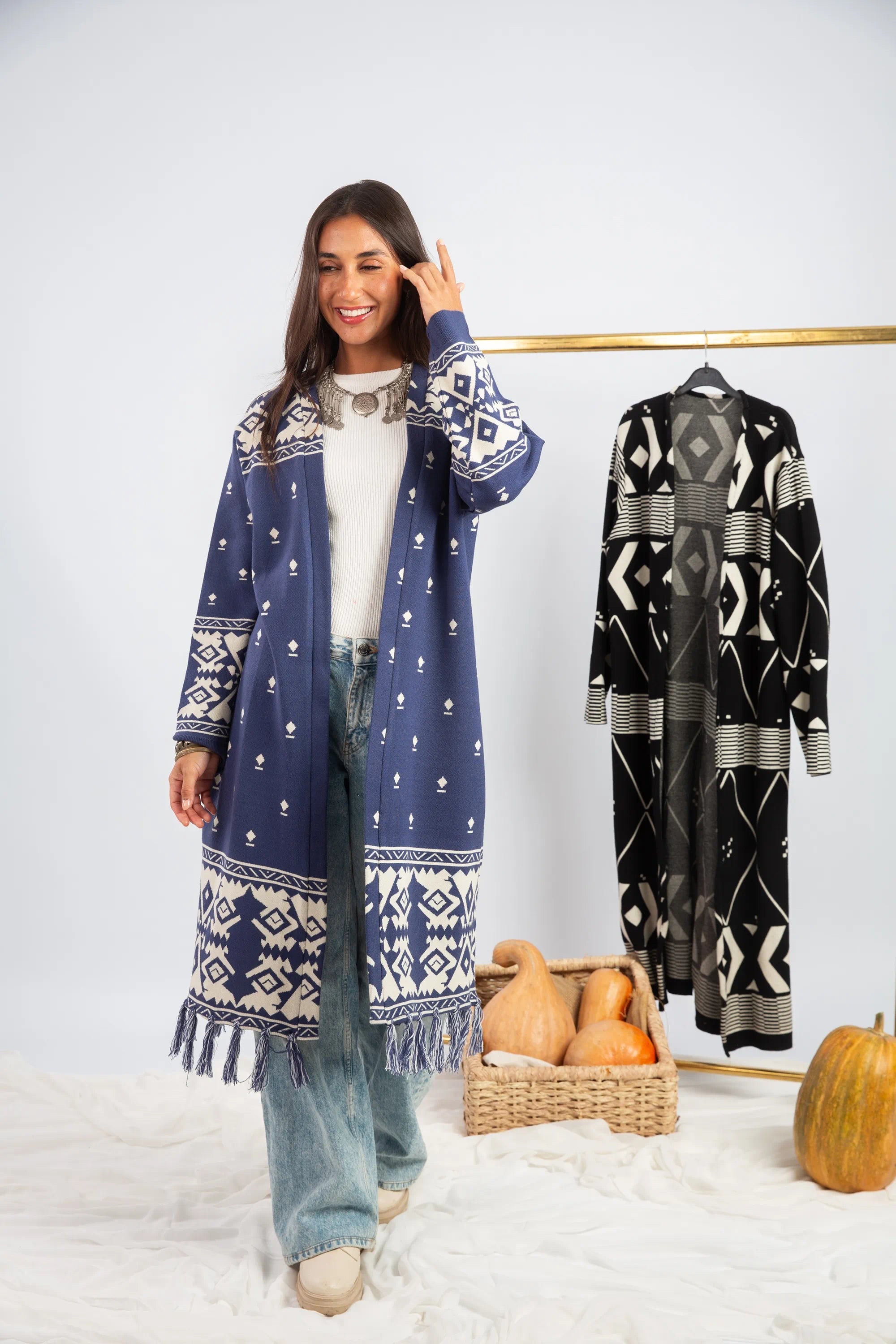 Woman wearing a blue patterned dress with a matching coat, standing next to a rack of similar clothing.