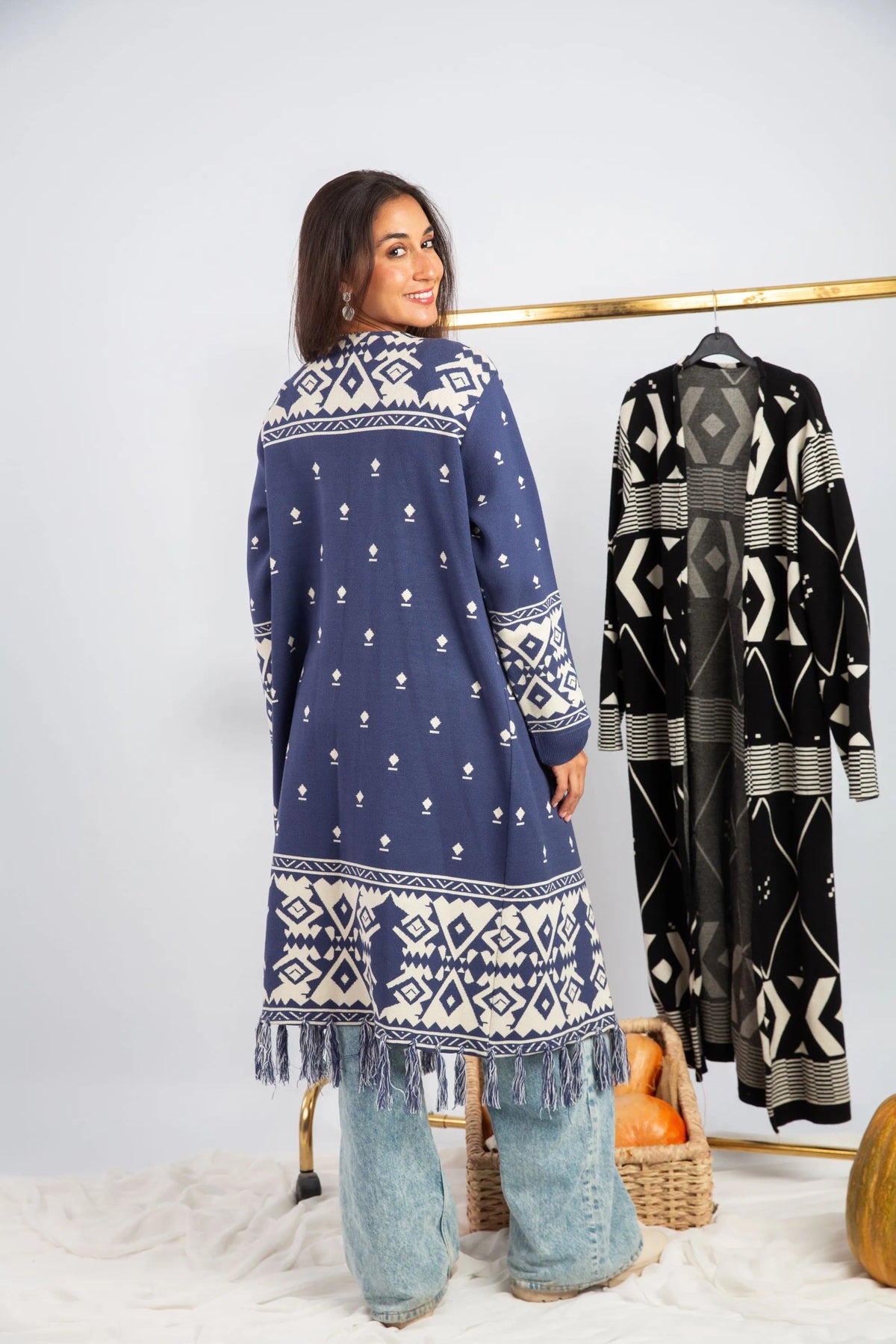 Woman wearing a blue patterned dress with a black and white patterned coat in the background.