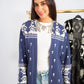 Woman wearing a blue patterned cardigan with a white shirt and jeans, standing in front of a clothing rack.