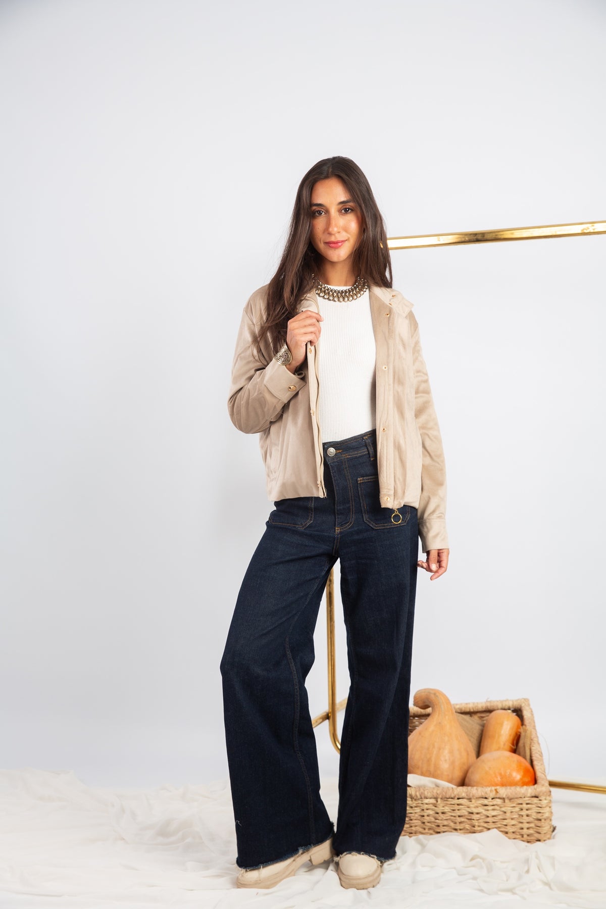 Woman in beige cardigan and dark jeans holding a basket with pumpkins on a white background