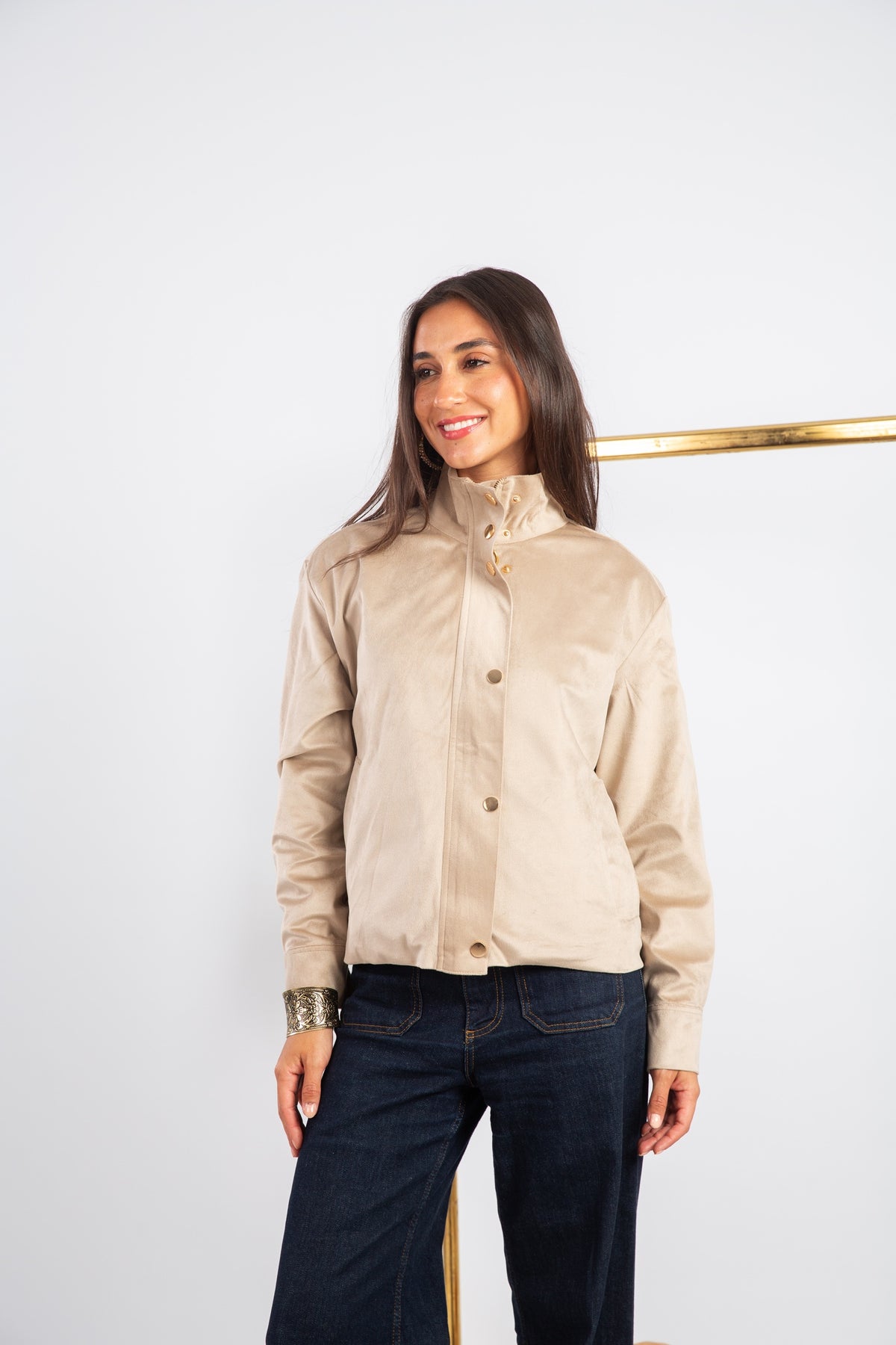Woman wearing a beige shirt and dark jeans against a white background