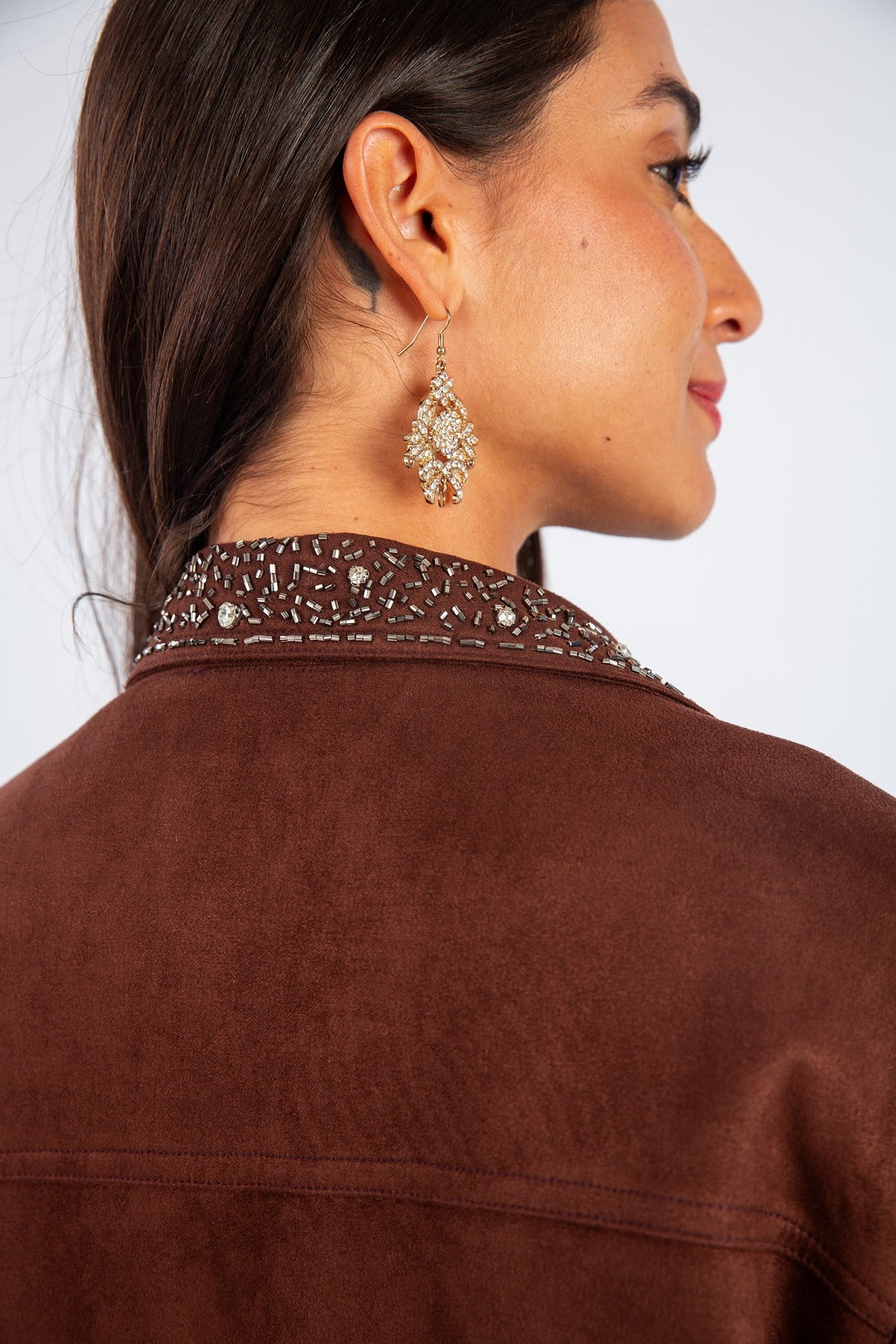 Woman wearing a brown jacket with decorative collar and earrings on a white background