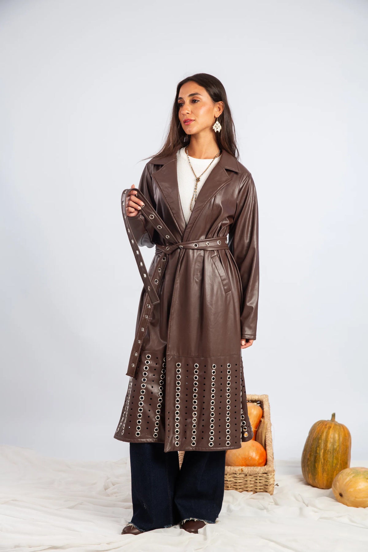 Woman wearing a brown leather trench coat with pumpkins and a basket on a white background