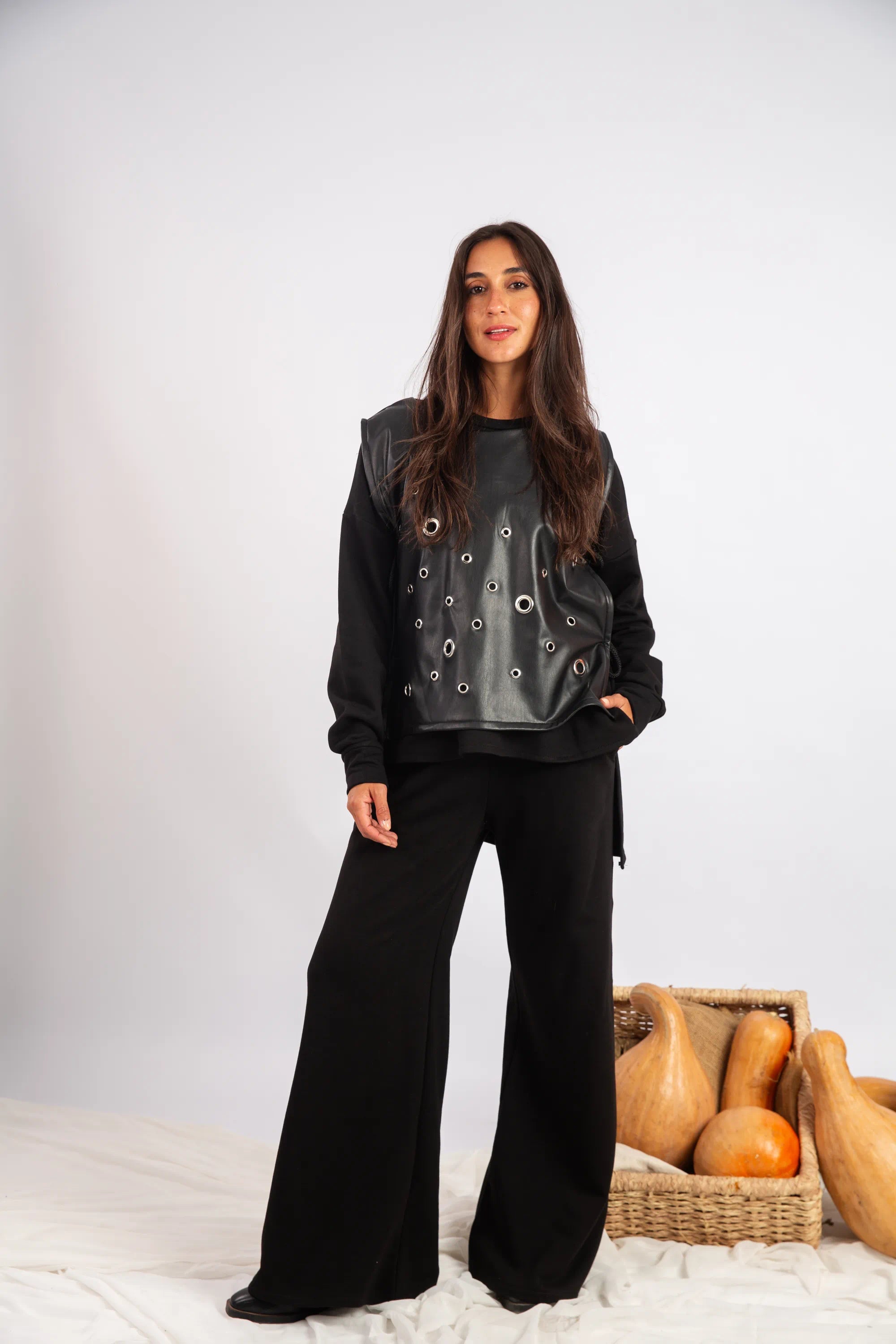 Woman wearing a black outfit with a textured top, standing against a white background with wooden objects.
